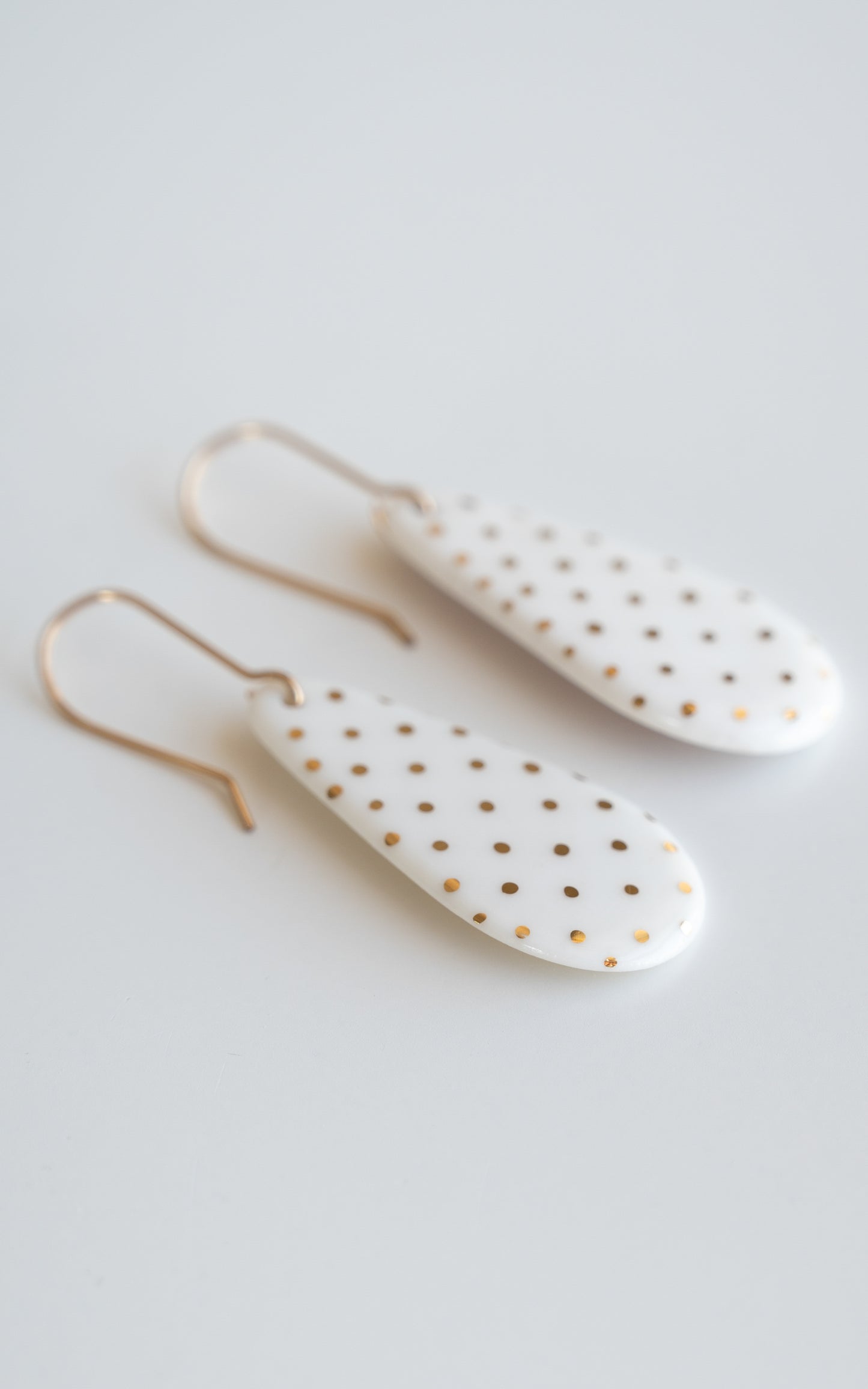 Drop earrings / S by Rozenthal Jewelry: white teardrop-shaped porcelain statement earrings with small gold dots and gold hooks, handmade in Latvia and shown on a white surface.