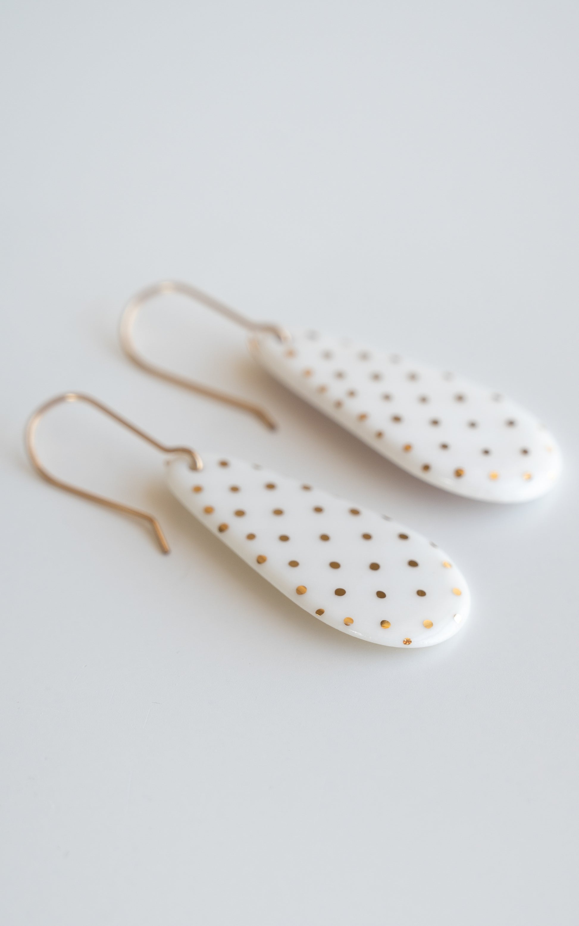 Drop earrings / S by Rozenthal Jewelry: white teardrop-shaped porcelain statement earrings with small gold dots and gold hooks, handmade in Latvia and shown on a white surface.