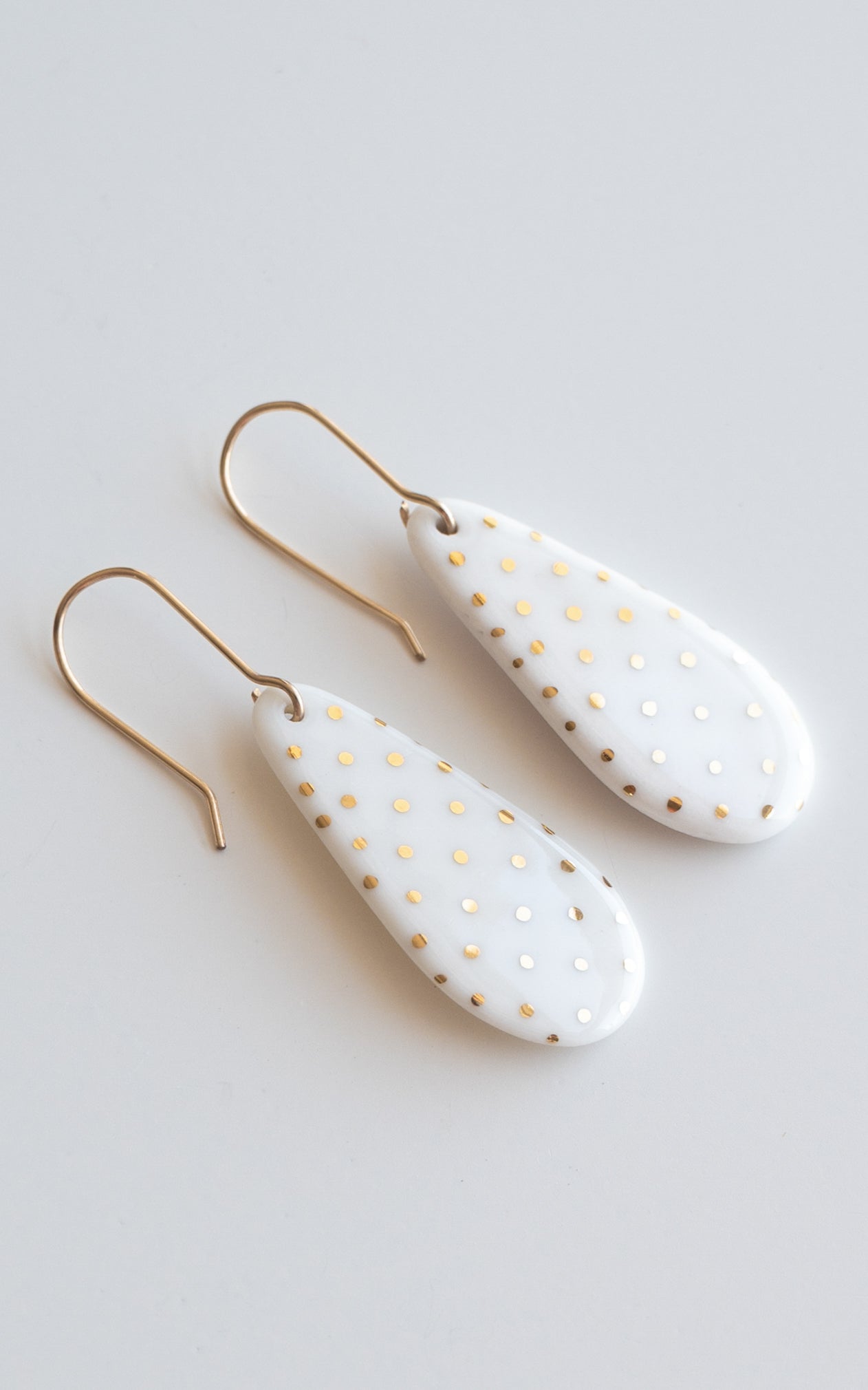 Rozenthal Jewelry Drop earrings / S: Teardrop-shaped white lightweight waterproof earrings with gold polka dots and hooks, shown on a light gray surface.