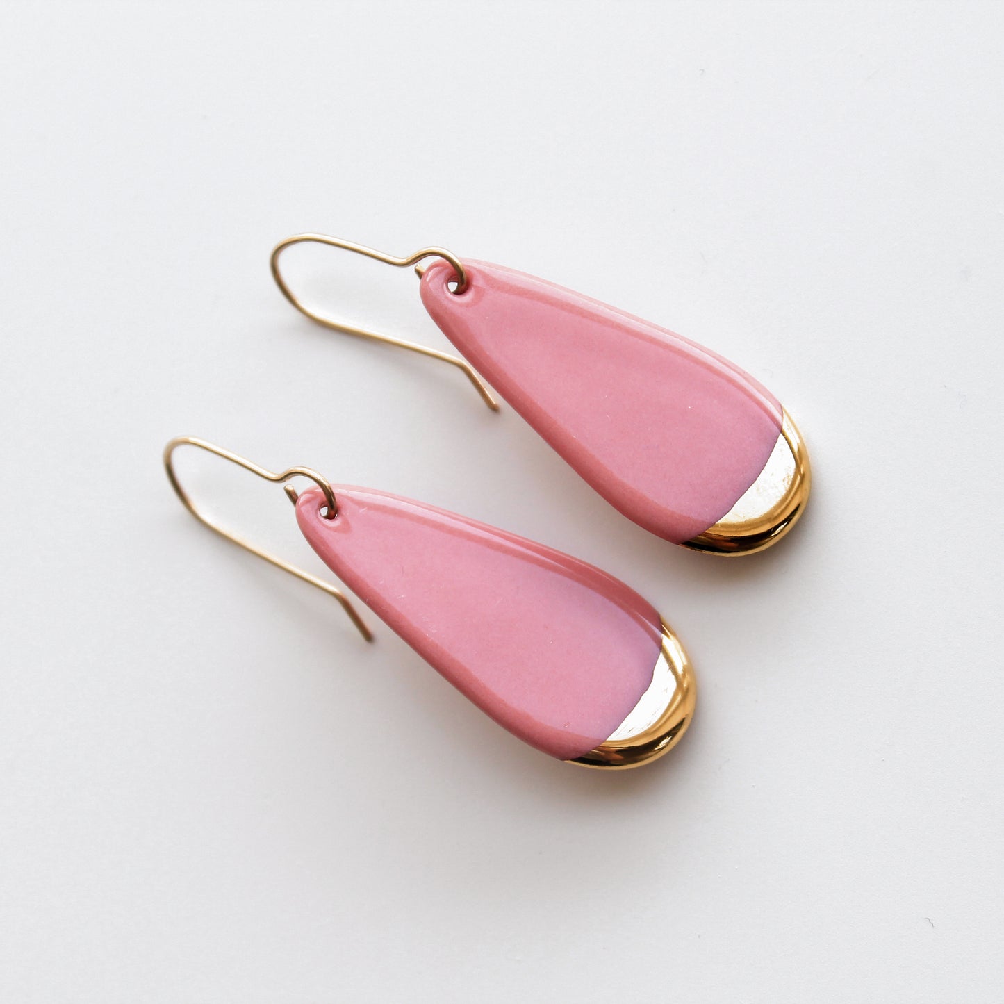 Drop earrings / S by Rozenthal Jewelry are teardrop-shaped with pink enamel and gold-toned edges, featuring simple gold hooks. Handmade in Latvia, these hypoallergenic designer earrings are shown on a white background.