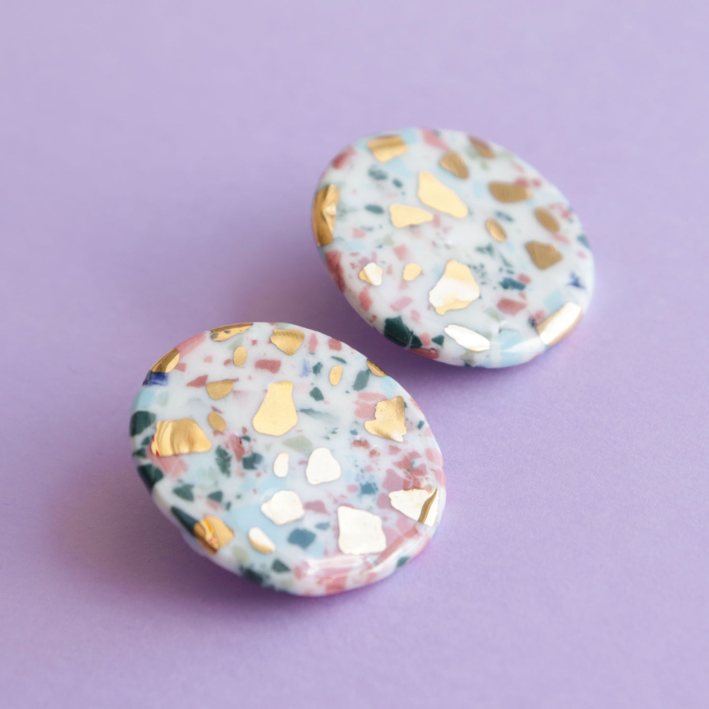 Astilla Recycled Studs / M by Rozenthal Jewelry: round terrazzo-style earrings with pink, blue, and green speckles plus gold foil accents—perfect for handmade jewelry lovers. Shown on a light purple background.