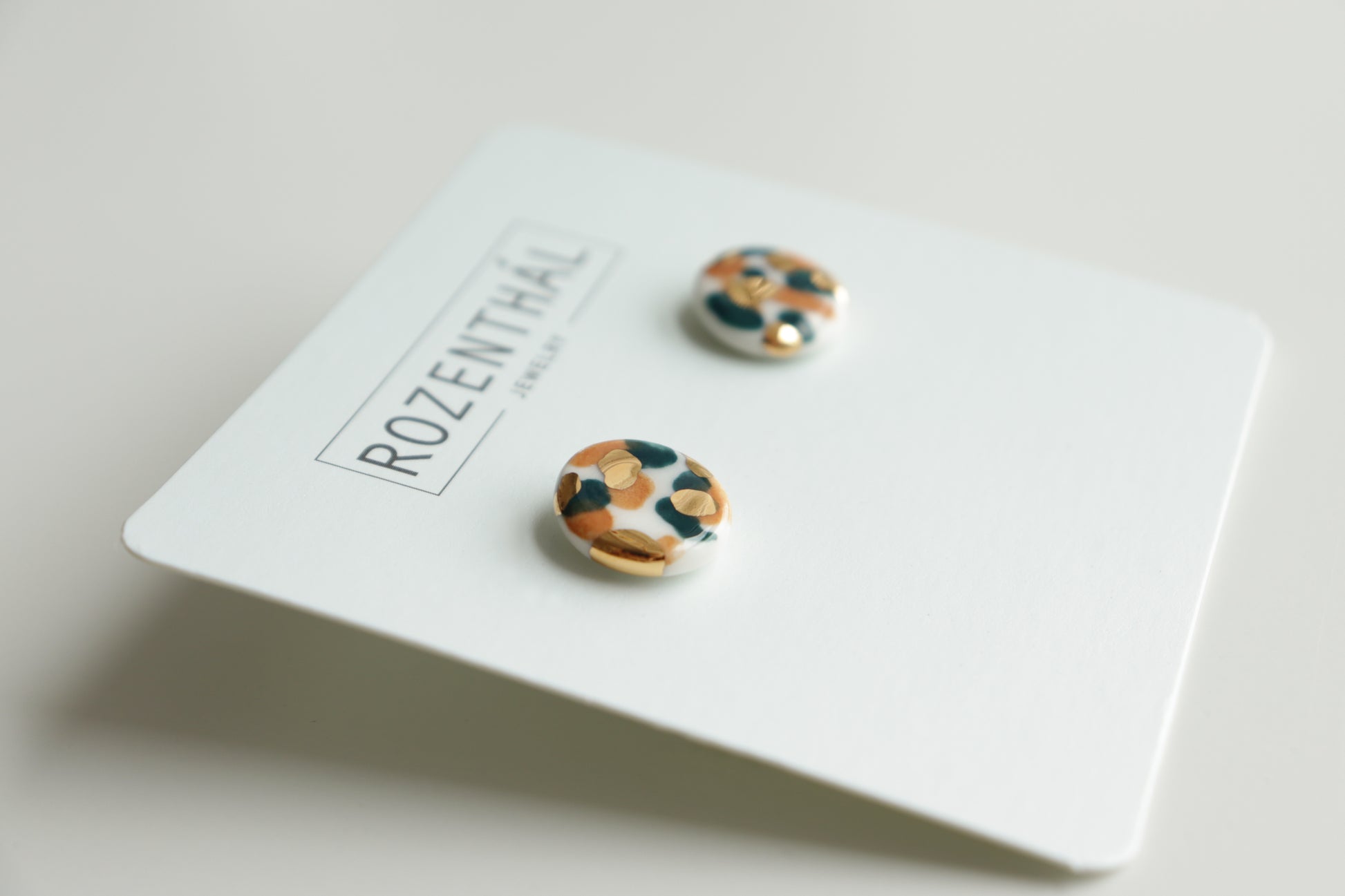 Handmade in Latvia, the Tache Studs / S by Rozenthal Jewelry are round, multicolored stud earrings with abstract patterns, shown on a white card labeled ROZENTHAL.