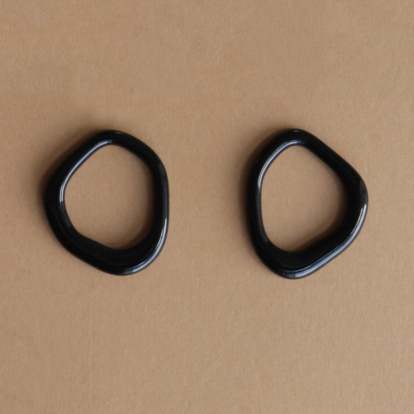 The Arp Pearl Hoops by Rozenthal Jewelry, two uniquely shaped black earrings, are displayed side by side on a plain light brown surface.