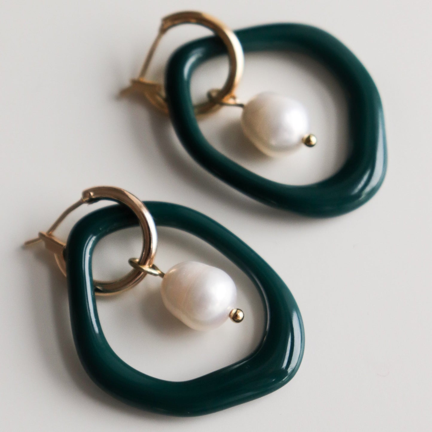 The Arp Pearl Hoops by Rozenthal Jewelry are handmade earrings featuring irregular dark green hoops, gold closures, and large white freshwater pearl-like beads for a strikingly modern look.