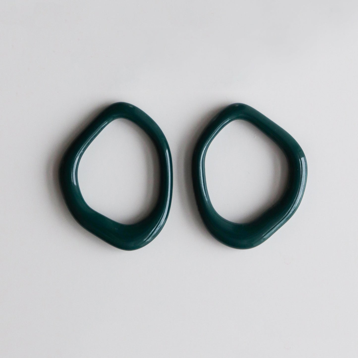 Two irregularly shaped dark green Arp Pearl Hoops by Rozenthal Jewelry are displayed side by side on a plain white background.