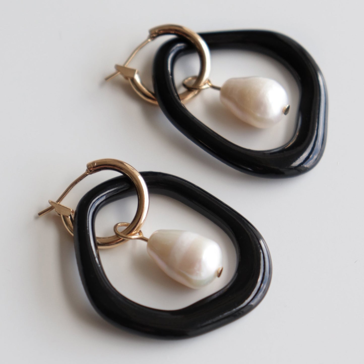 The Arp Pearl Hoops by Rozenthal Jewelry are freshwater pearl earrings with irregular black hoops, small gold hoops, and dangling white teardrop pearls, shown on a plain white surface.