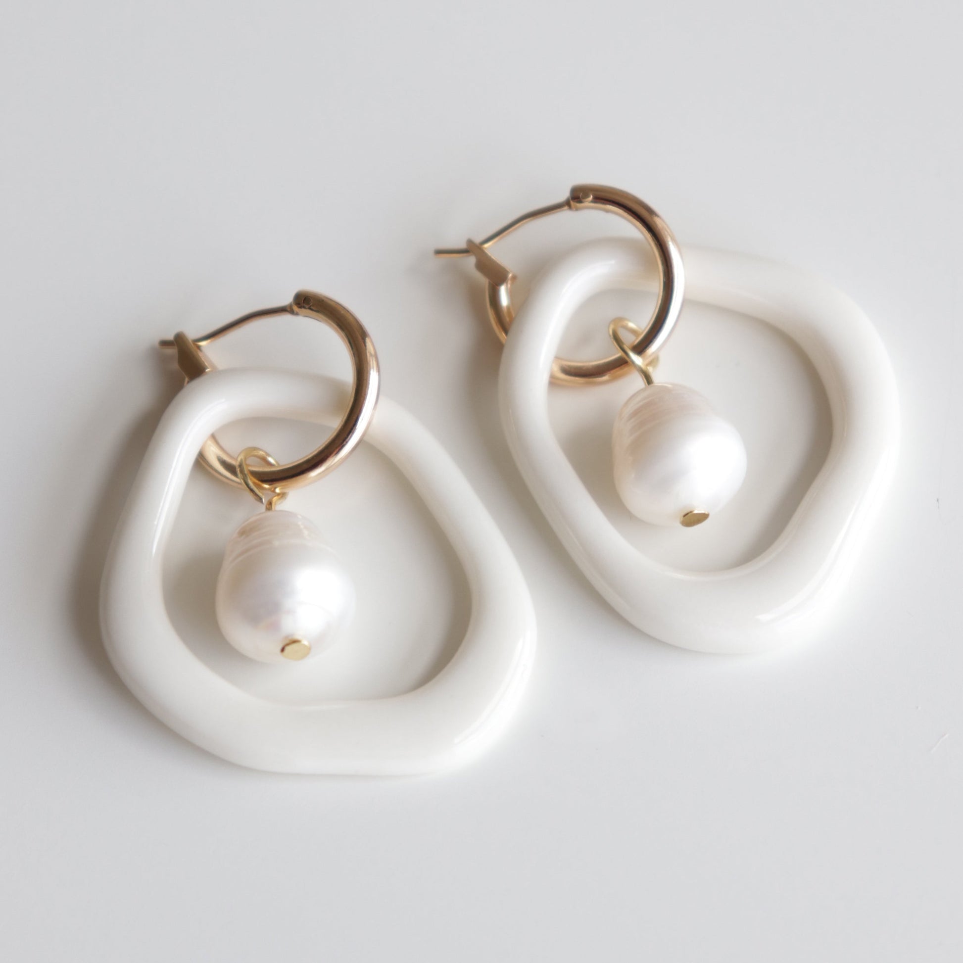 The Arp Pearl Hoops by Rozenthal Jewelry feature gold hoops with irregular white oval frames and dangling round freshwater pearls, shown on a plain white background.