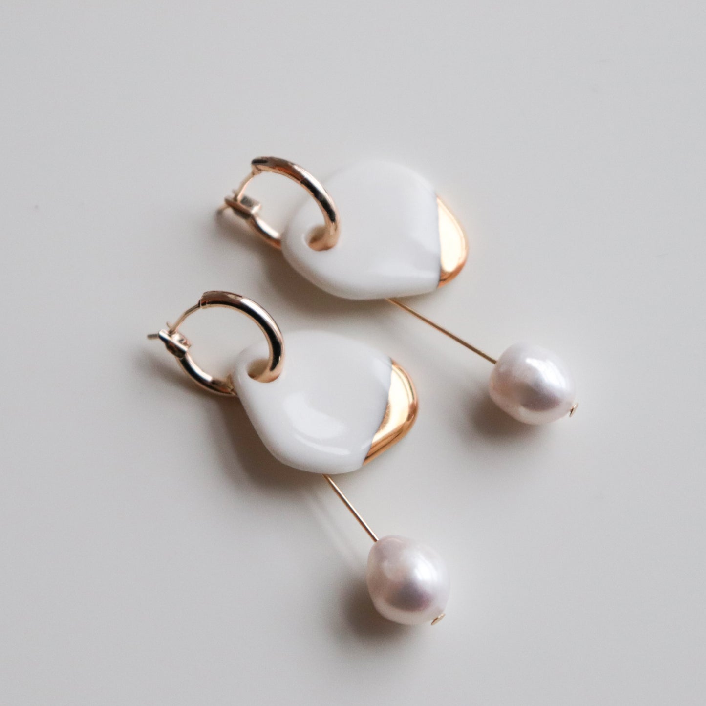 Arp Pearl Hoops by Rozenthal Jewelry—handmade earrings with gold hoops, white enamel heart accents, and dangling freshwater pearls. Perfect for lovers of unique jewelry. Displayed on a white surface.