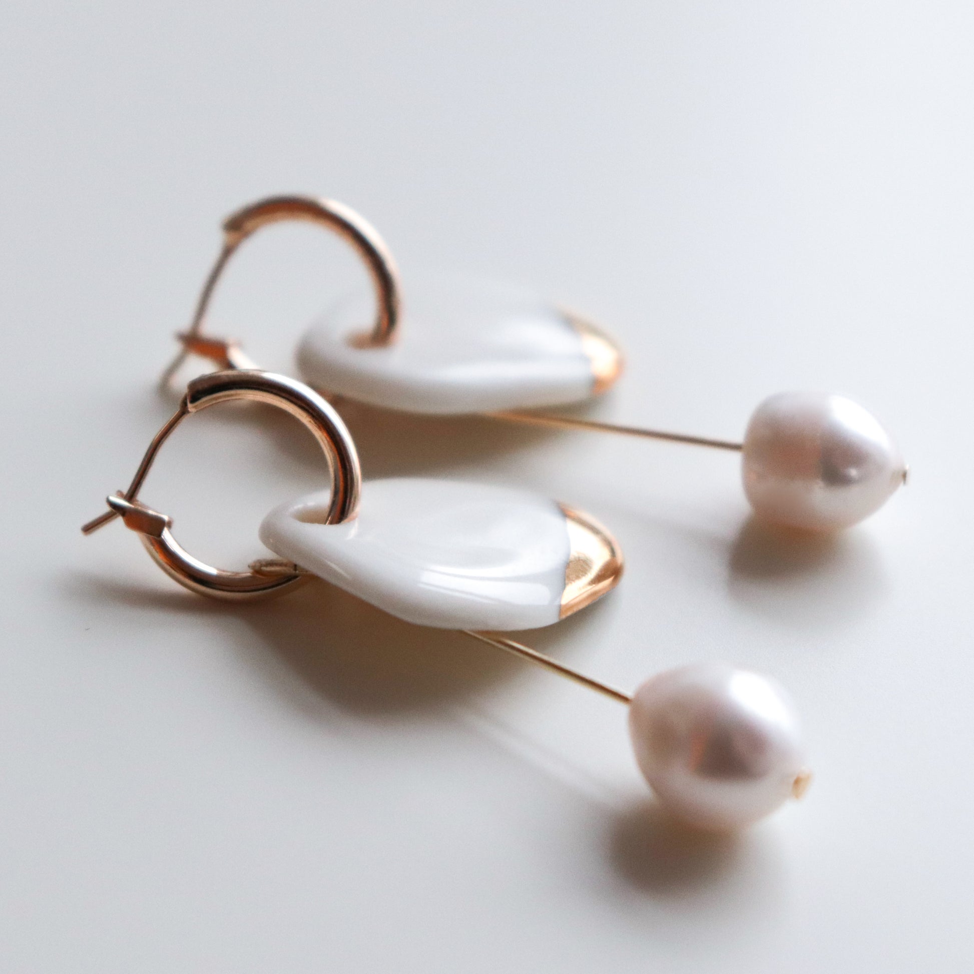 The Arp Pearl Hoops by Rozenthal Jewelry are elegant handmade earrings with gold hoops, white shell-like accents, and dangling freshwater pearl beads, beautifully displayed on a white surface.