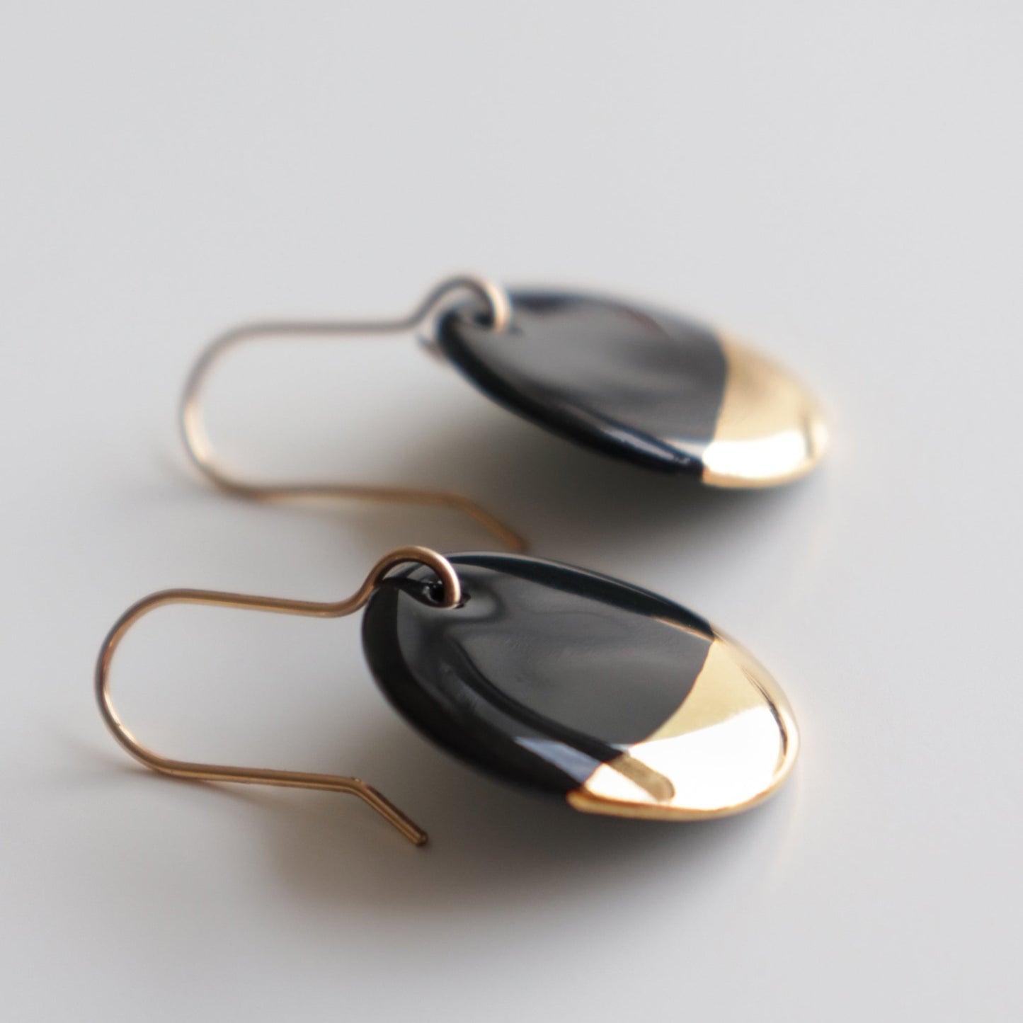 Rozenthal Jewelrys Round Earrings feature minimalist black and gold pendants on simple gold hooks, elegantly displayed against a light, neutral background—an understated accessory for any style.