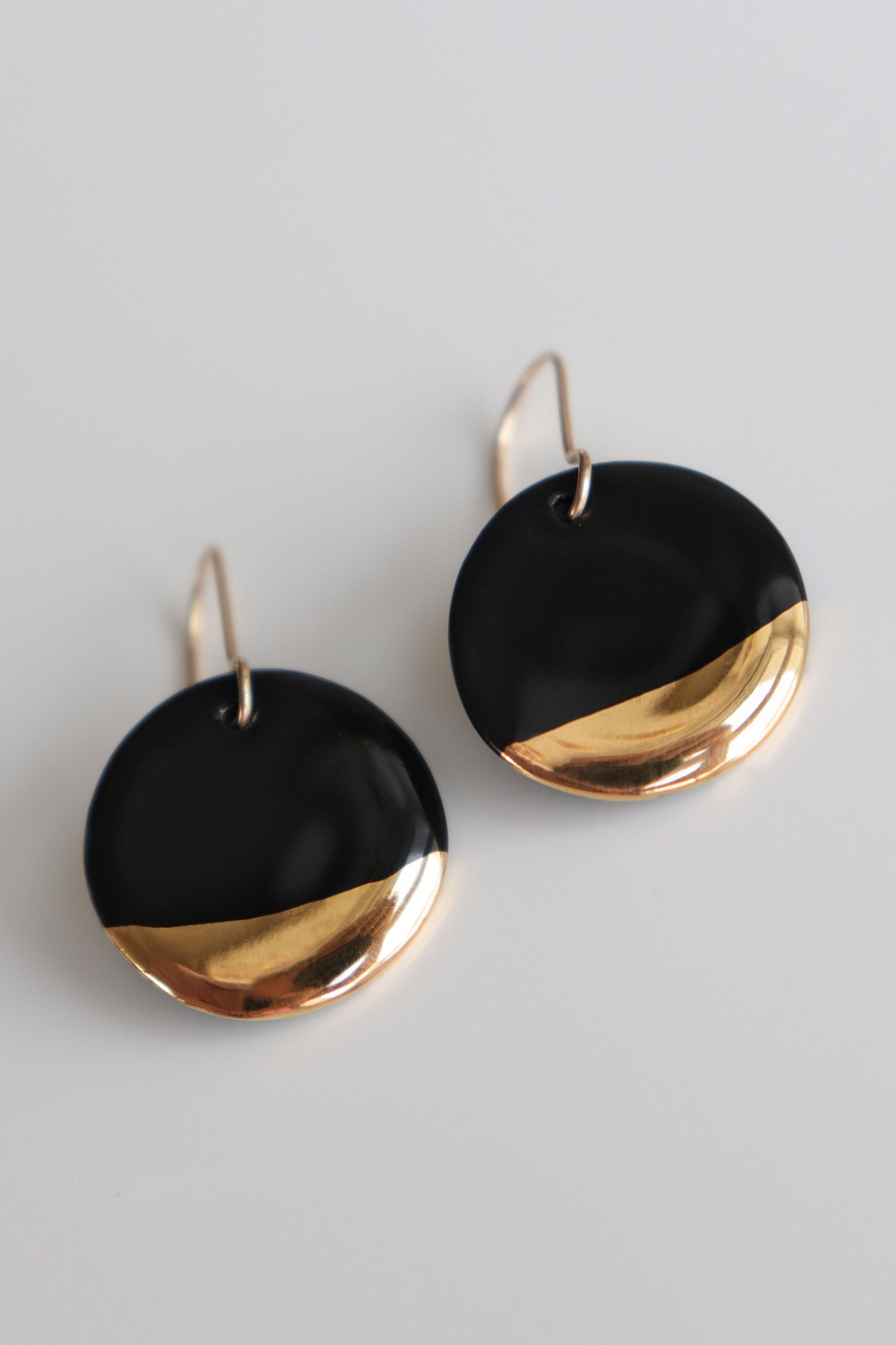 The Round Earrings by Rozenthal Jewelry are minimalist dangle earrings with black and gold color blocking, showcasing a glossy black top and shiny gold bottom. Displayed on a white background.