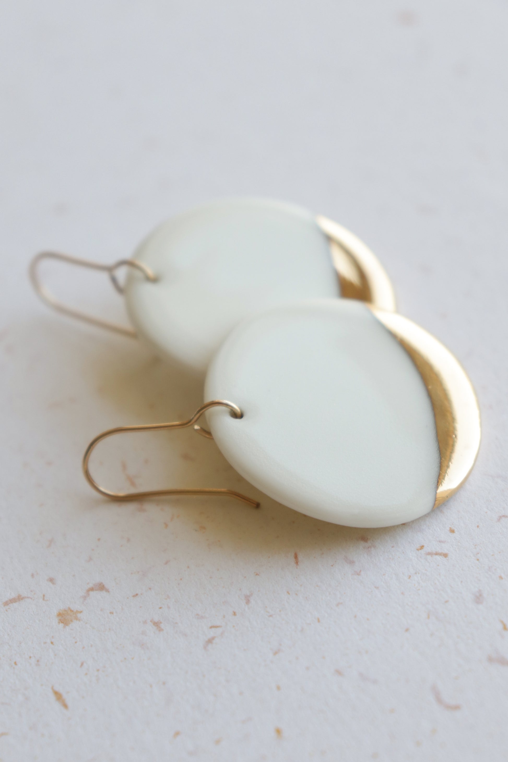 Round Earrings by Rozenthal Jewelry—handmade with white ceramic pieces, gold metal semicircle accents, and gold hooks. Minimalist design makes them an ideal choice for understated elegance.