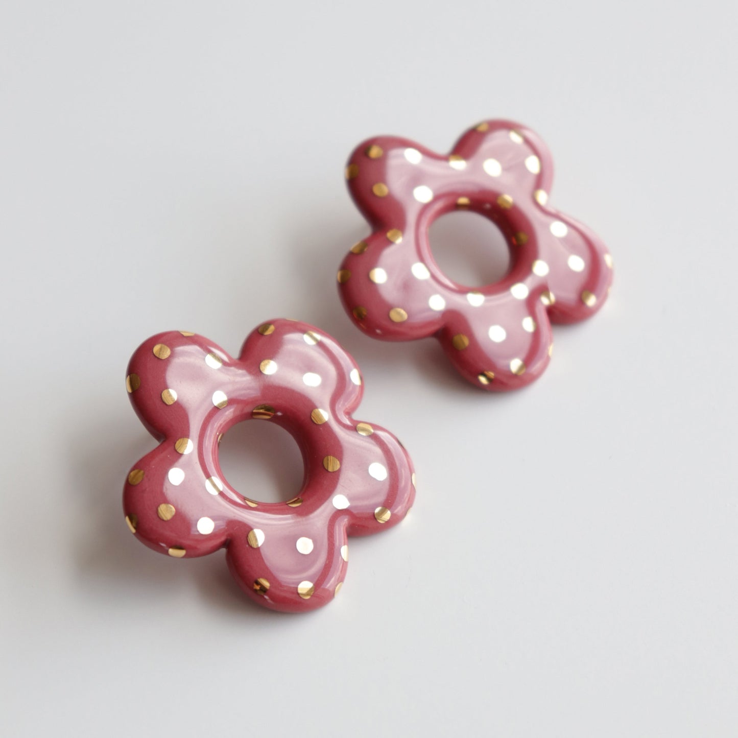 Pink flower-shaped earrings with gold polka dots on a light gray background