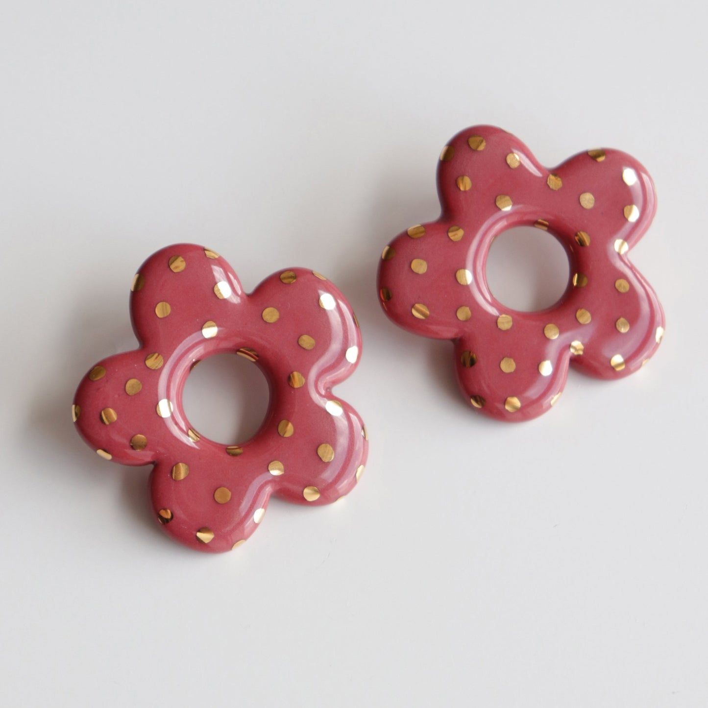 Pair of pink flower-shaped earrings with gold polka dots on a light gray background