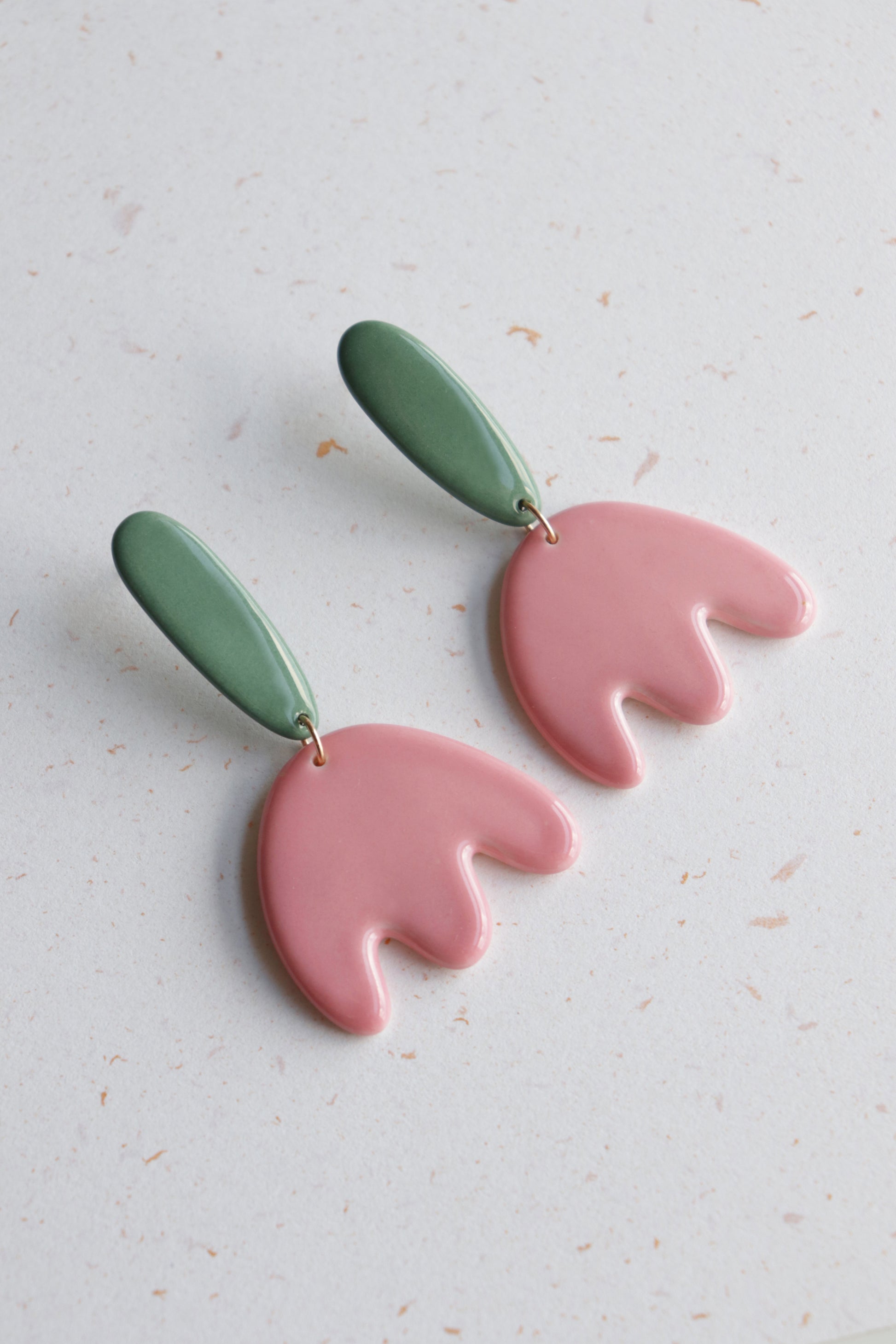 Tulip Earrings by Rozenthal Jewelry: handmade flower earrings featuring green oval studs and pink abstract petal dangles, shown on a light speckled surface.