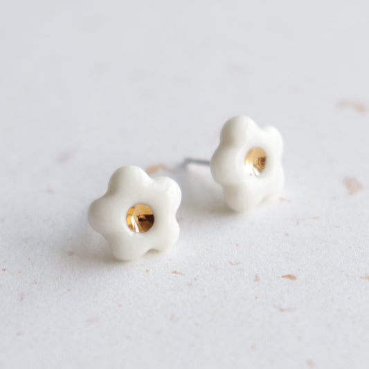 Rozenthal Jewelry’s Daisy Studs / XS are white, flower-shaped porcelain earrings with gold centers—handmade delicate jewelry for any occasion, shown on a light speckled surface.