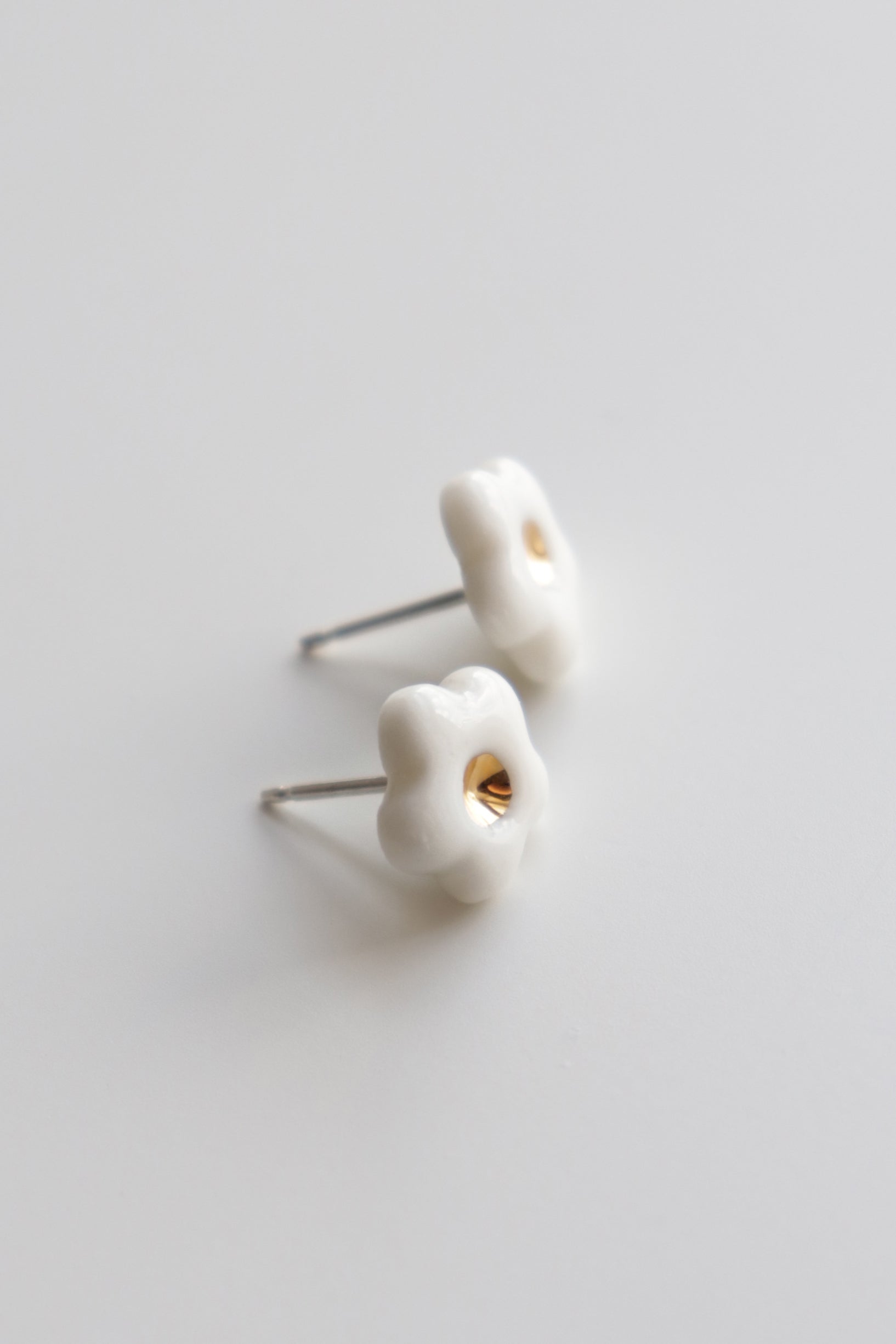 Two small Daisy Studs / XS by Rozenthal Jewelry, handmade white flower-shaped earrings with gold centers, are displayed on a smooth, light-colored surface.