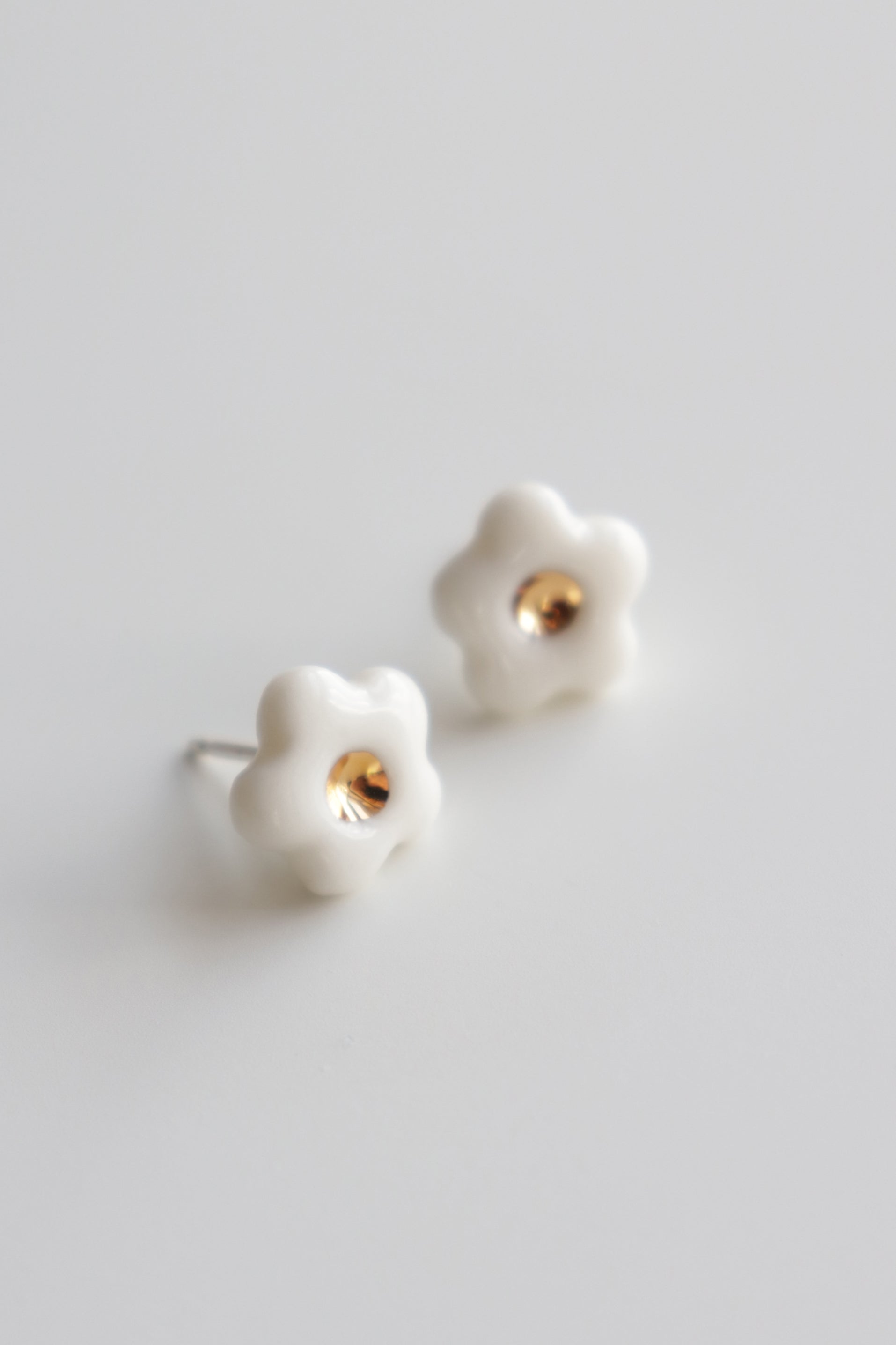 The Daisy Studs / XS by Rozenthal Jewelry are white, flower-shaped porcelain handmade earrings with a small gold center, shown on a plain light background.