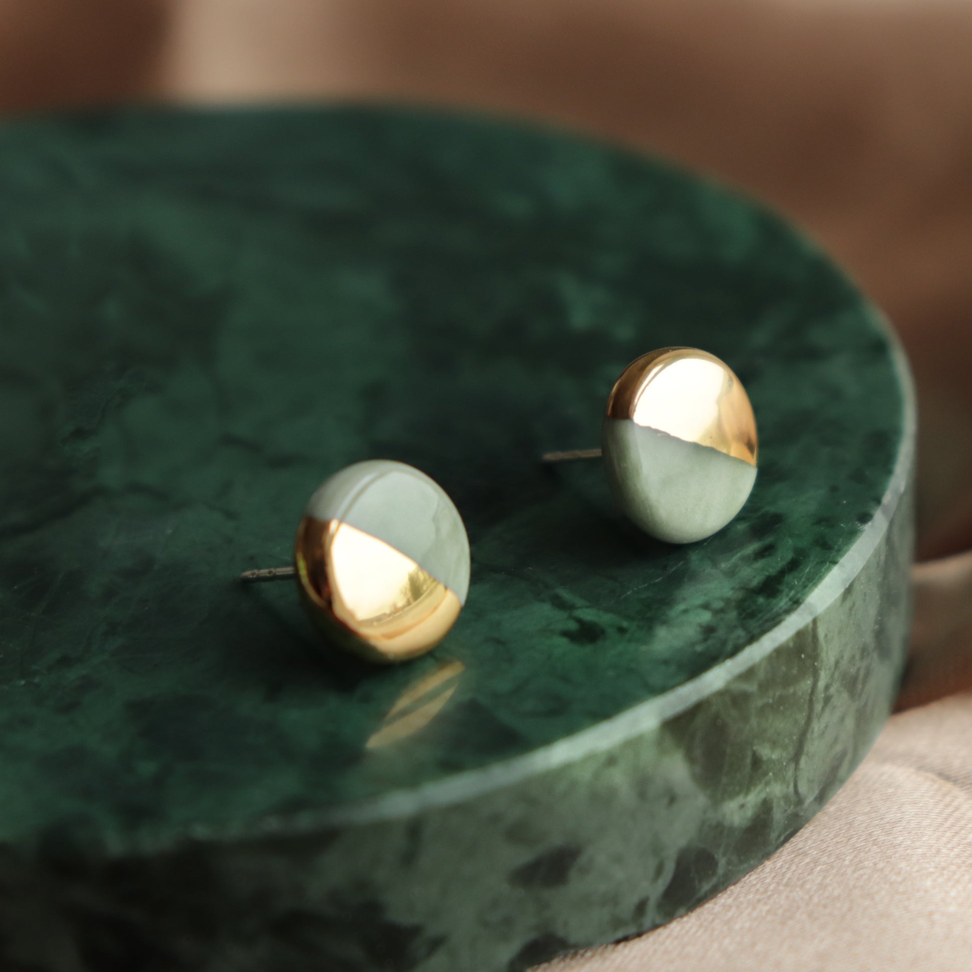 Round Studs / XS by Rozenthal Jewelry: minimalist round stud earrings featuring a diagonal gold and matte silver design, showcased on polished green marble.