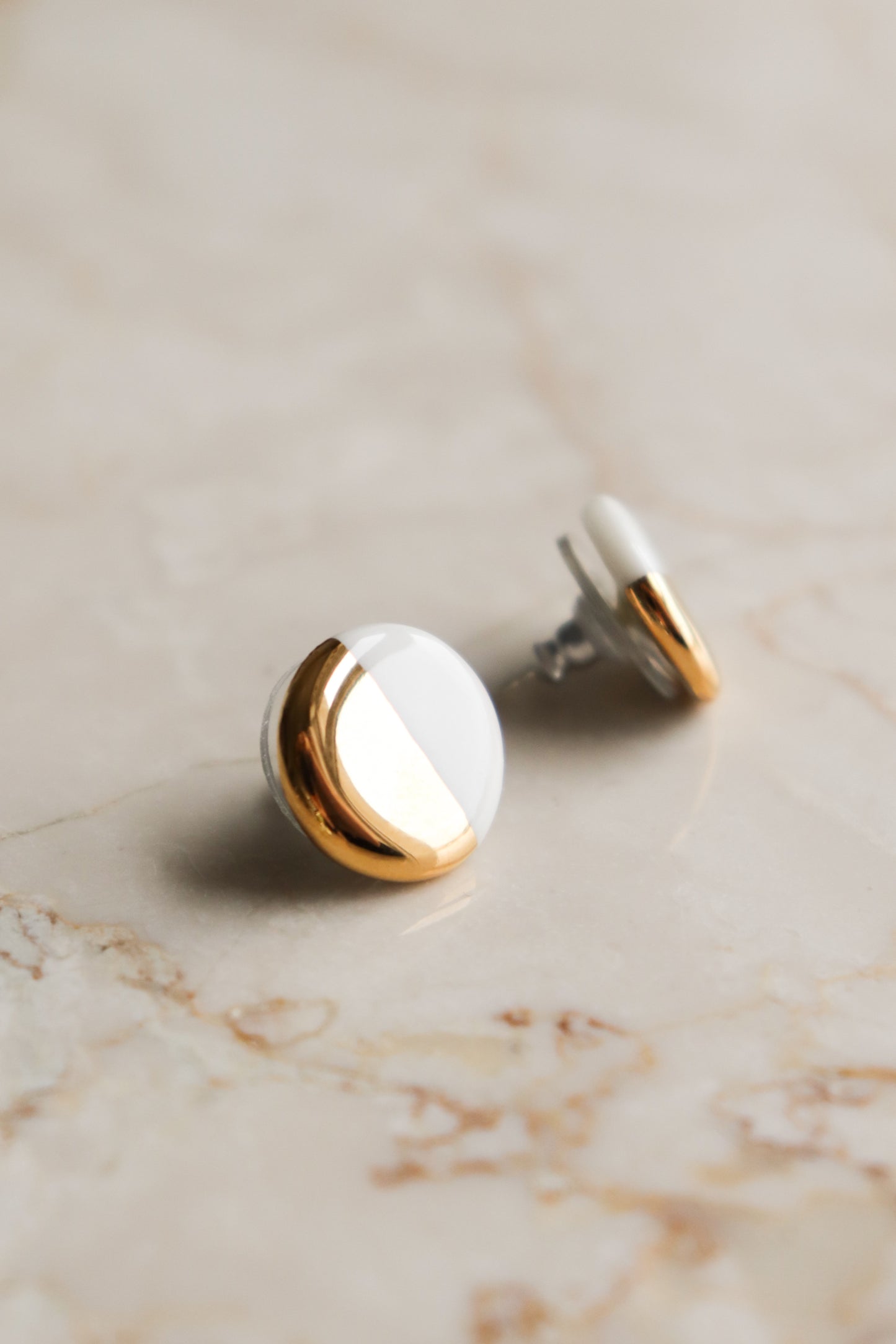 The Round Studs / S by Rozenthal Jewelry feature a half gold, half white enamel design, displayed on a light beige marble surface—ideal for minimalist jewelry lovers.