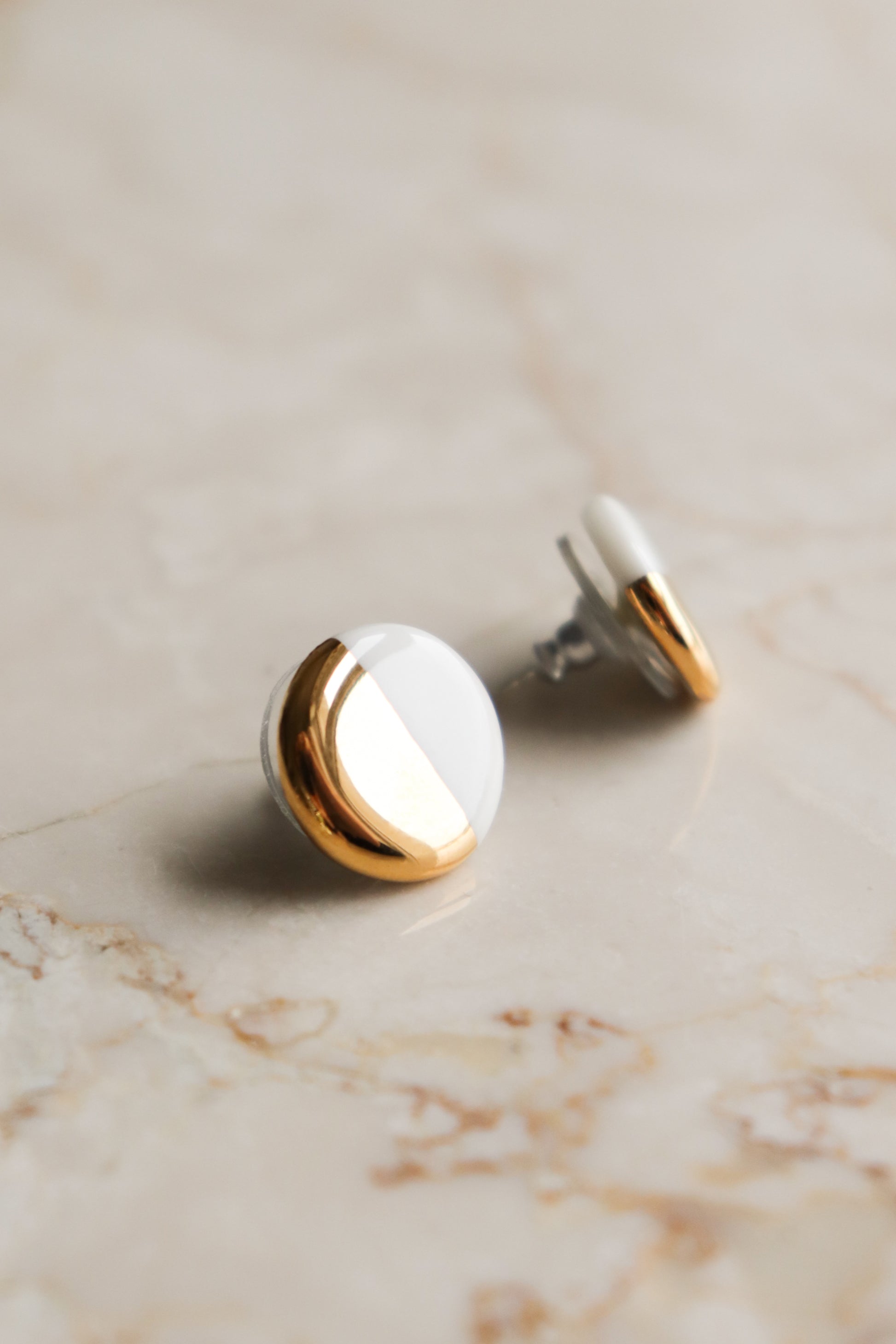 The Round Studs / S by Rozenthal Jewelry feature a half gold, half white enamel design, displayed on a light beige marble surface—ideal for minimalist jewelry lovers.
