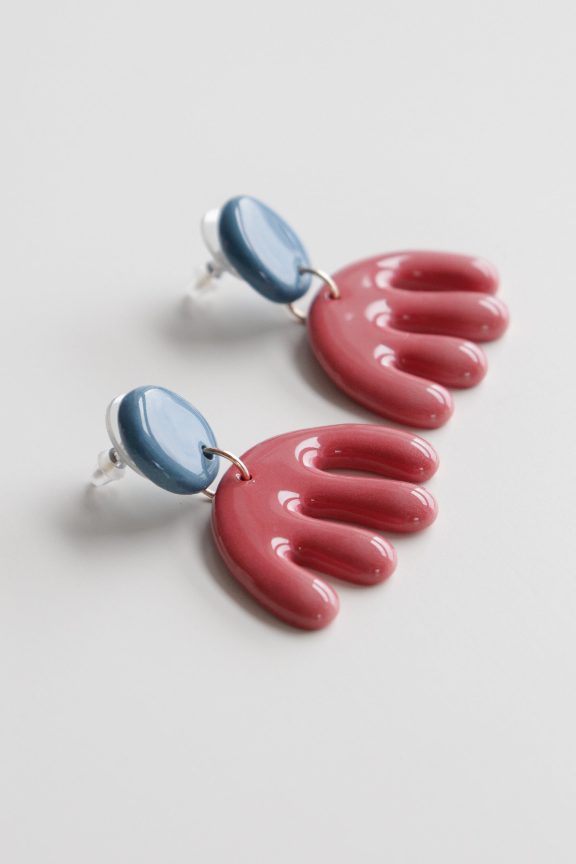 The Matisse Earrings by Rozenthal Jewelry are lightweight, waterproof earrings with blue circular studs and glossy red abstract fan-shaped dangles, handmade in Latvia and shown on a white background.