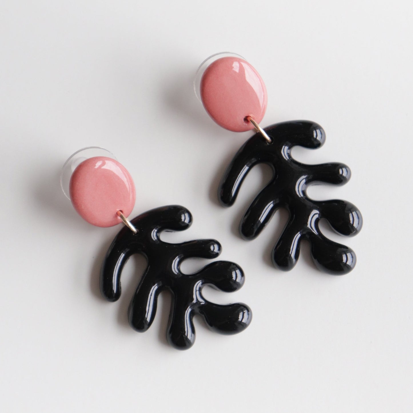 The Matisse Earrings by Rozenthal Jewelry are handmade, featuring round pink studs with dangling abstract black shapes, inspired by stylized leaves or coral.