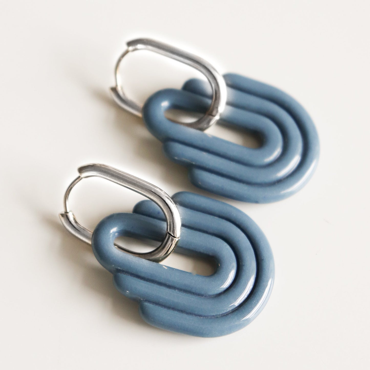 Art Deco Earrings by Rozenthal Jewelry feature handmade silver hoops with stacked blue U-shaped resin pendants, shown on a plain white background.