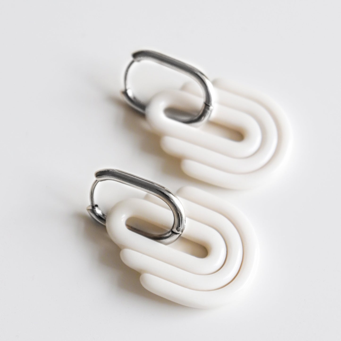 The Art Deco Earrings by Rozenthal Jewelry are modern, hypoallergenic designer earrings featuring silver hooks and white interlocking ovals, handmade in Latvia and shown on a plain white background.