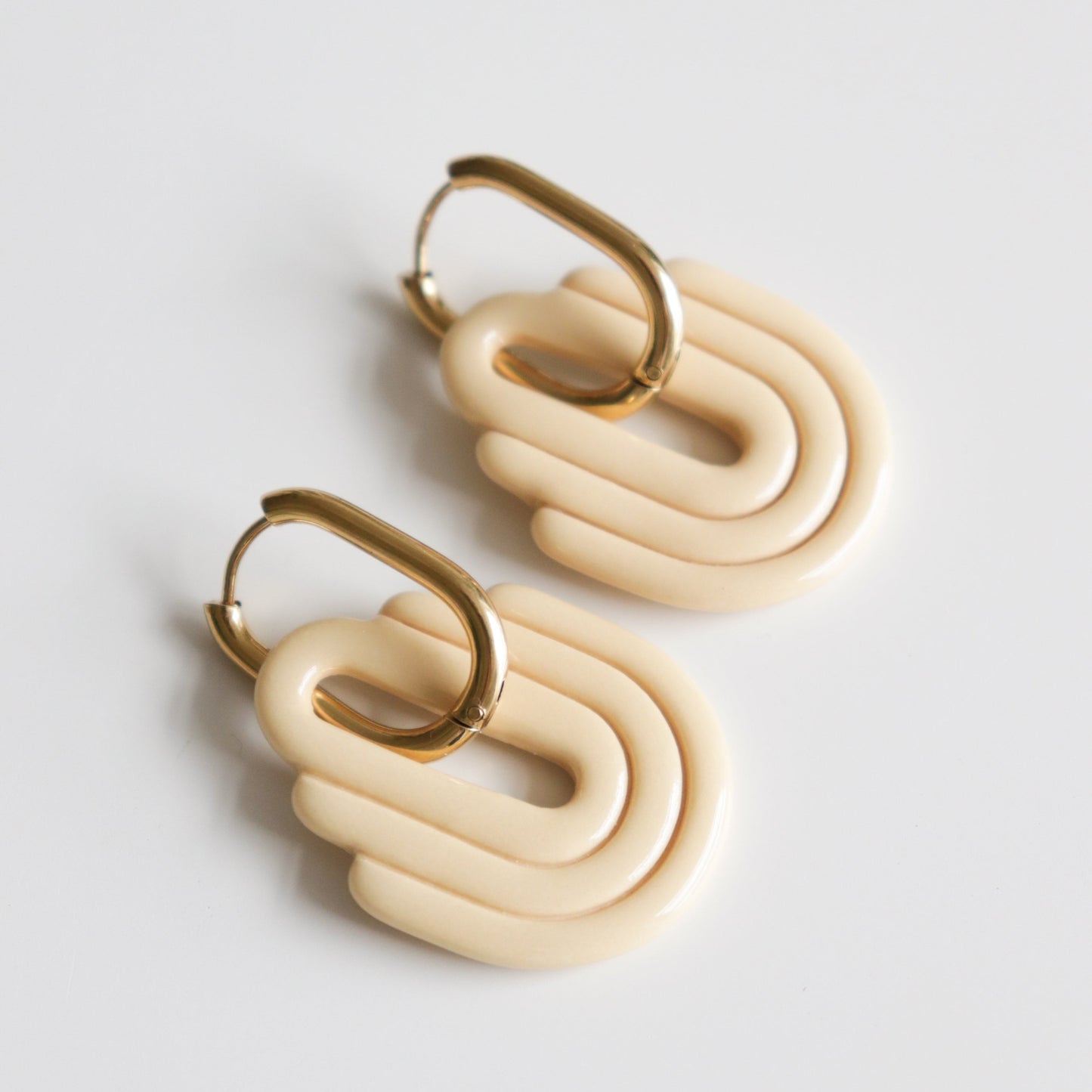 The Art Deco Earrings by Rozenthal Jewelry feature gold hoops with cream layered geometric pendants. Lightweight and waterproof, theyre perfect for everyday wear. Shown on a white background.