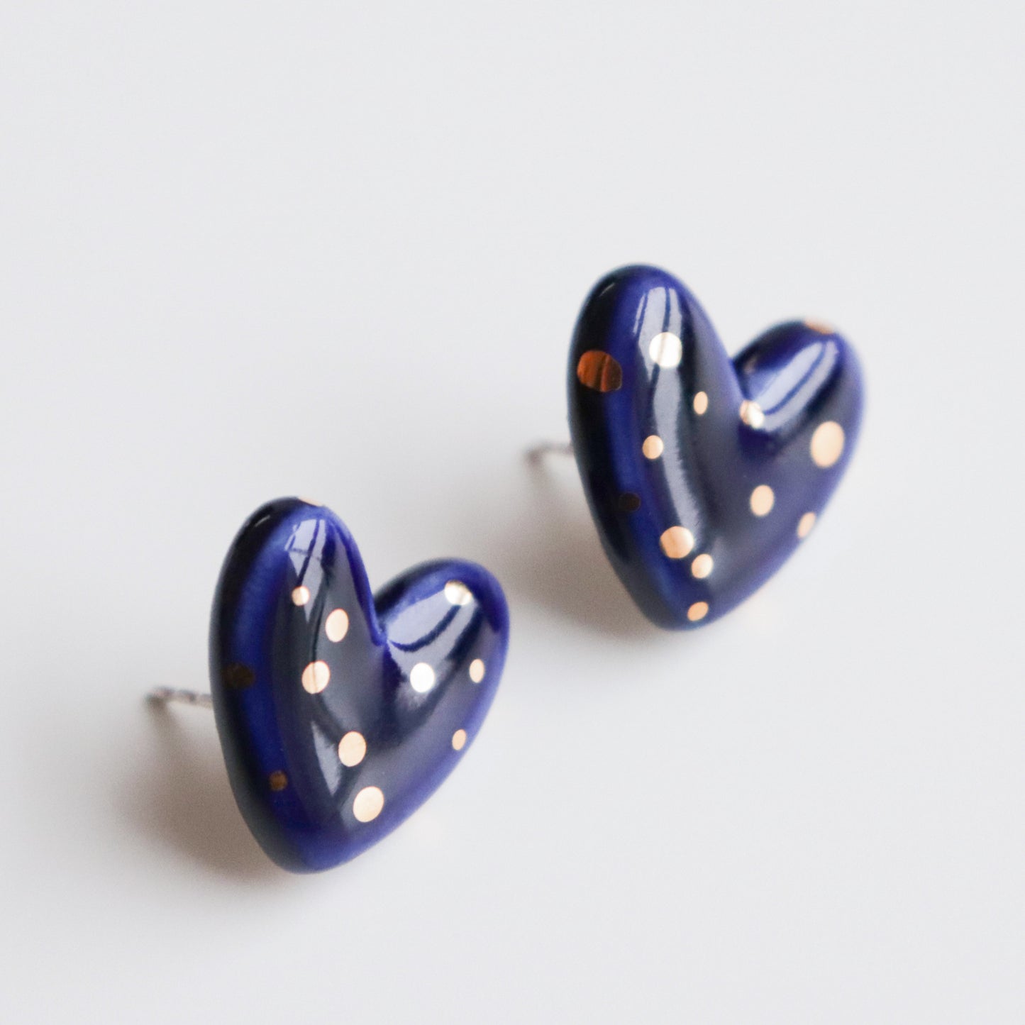 Heart Studs by Rozenthal Jewelry: dark blue, heart-shaped stud earrings with shiny gold polka dots, handmade in Latvia and shown on a white background.