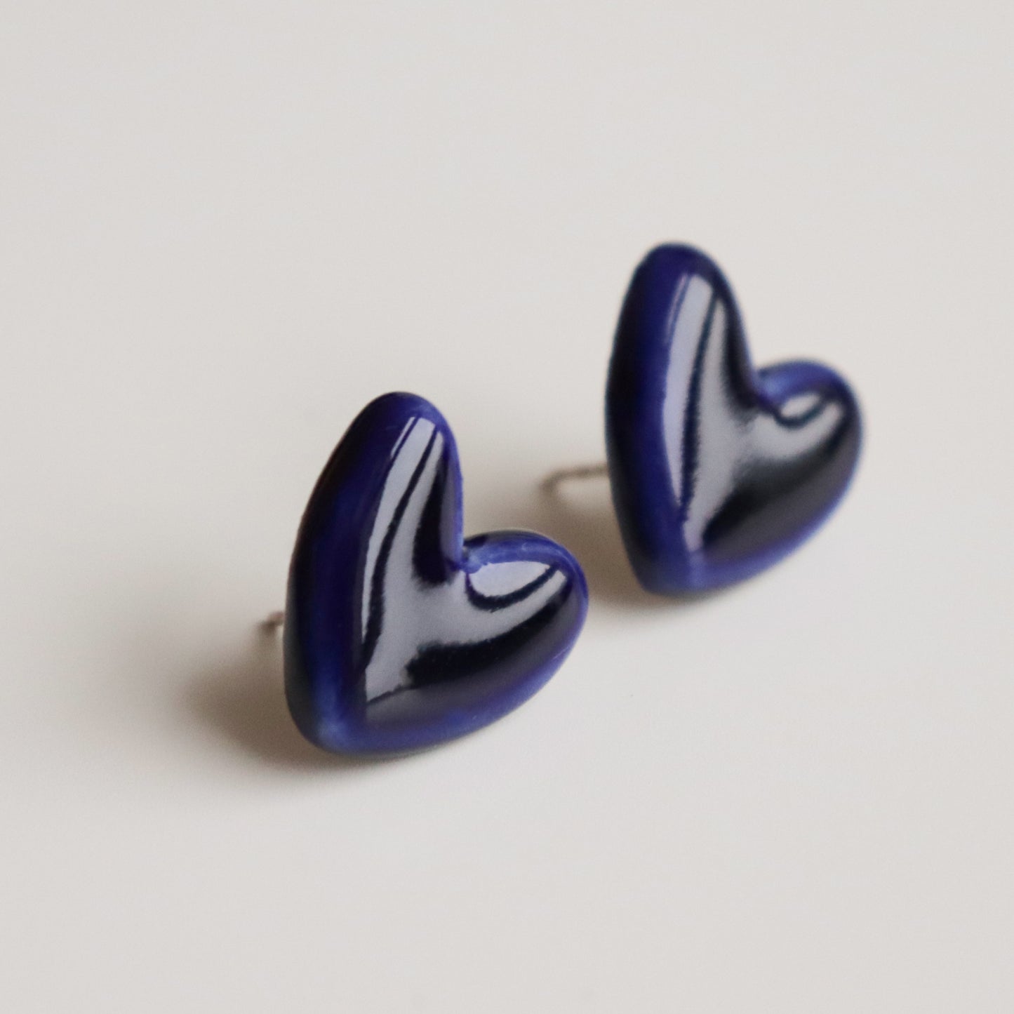Handmade in Latvia, the Heart Studs by Rozenthal Jewelry are glossy, dark blue heart-shaped earrings shown on a plain white background.