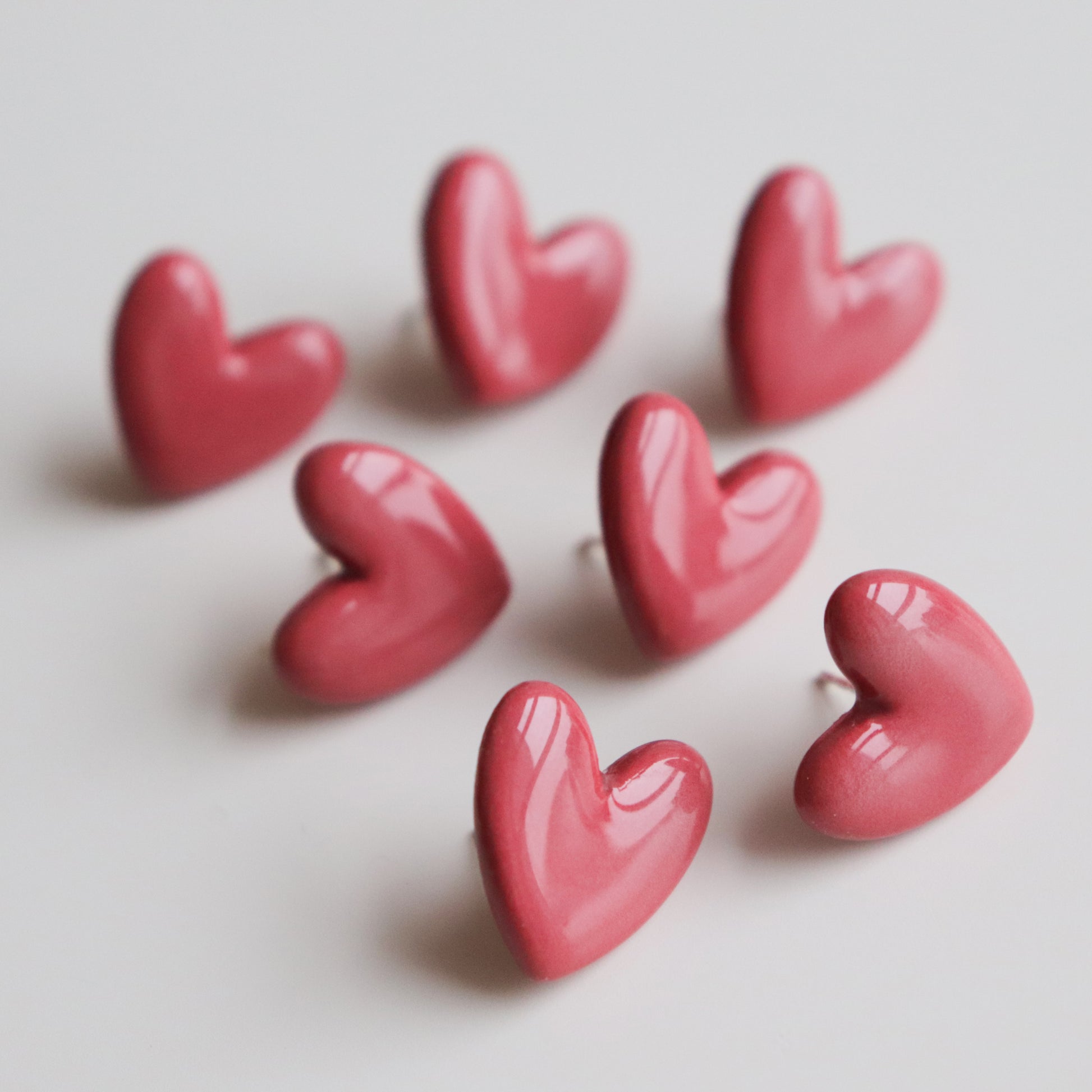 Seven small, glossy, pink Heart Studs by Rozenthal Jewelry are arranged in a loose cluster on a white surface, with their pointed ends facing various directions.