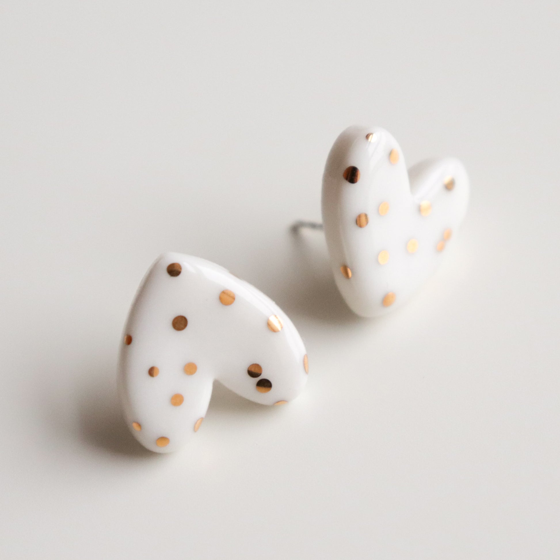 Heart Studs by Rozenthal Jewelry are handmade in Latvia—white, heart-shaped porcelain earrings with gold polka dots, displayed on a white surface.