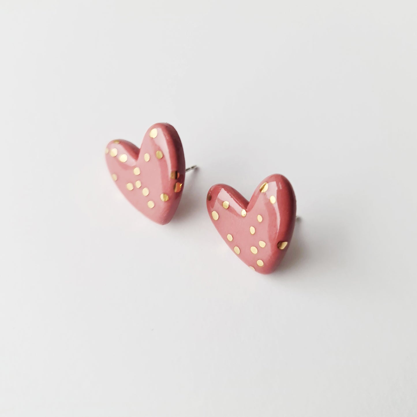 Heart Studs by Rozenthal Jewelry: pink, heart-shaped porcelain earrings with small gold polka dots. Lightweight, waterproof, and perfect for adding charm to any look. Displayed on a plain white background.