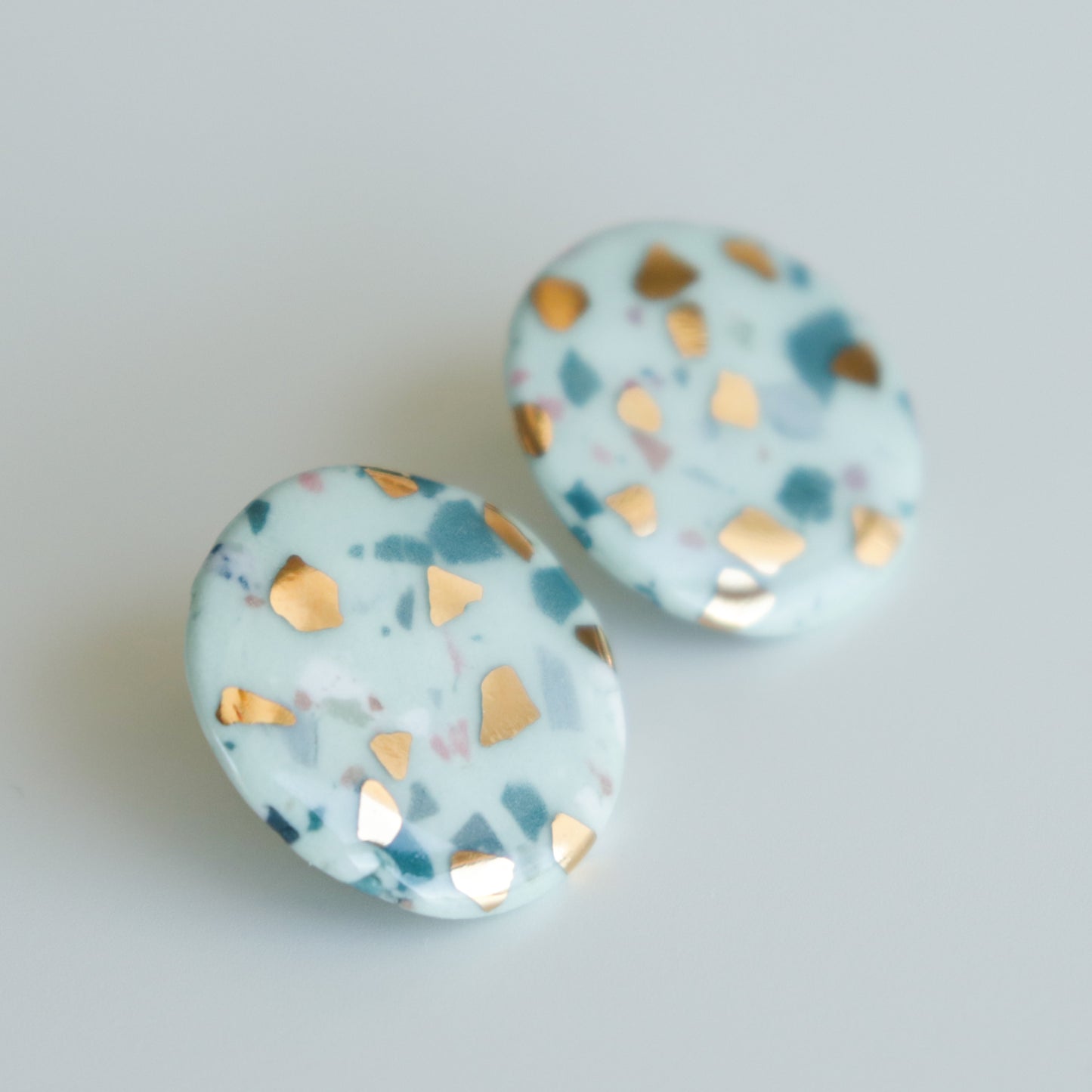 Astilla Recycled Studs / M by Rozenthal Jewelry: round, handmade earrings with a white base, blue and pink speckles, and shiny gold geometric accents shown on a plain light background.