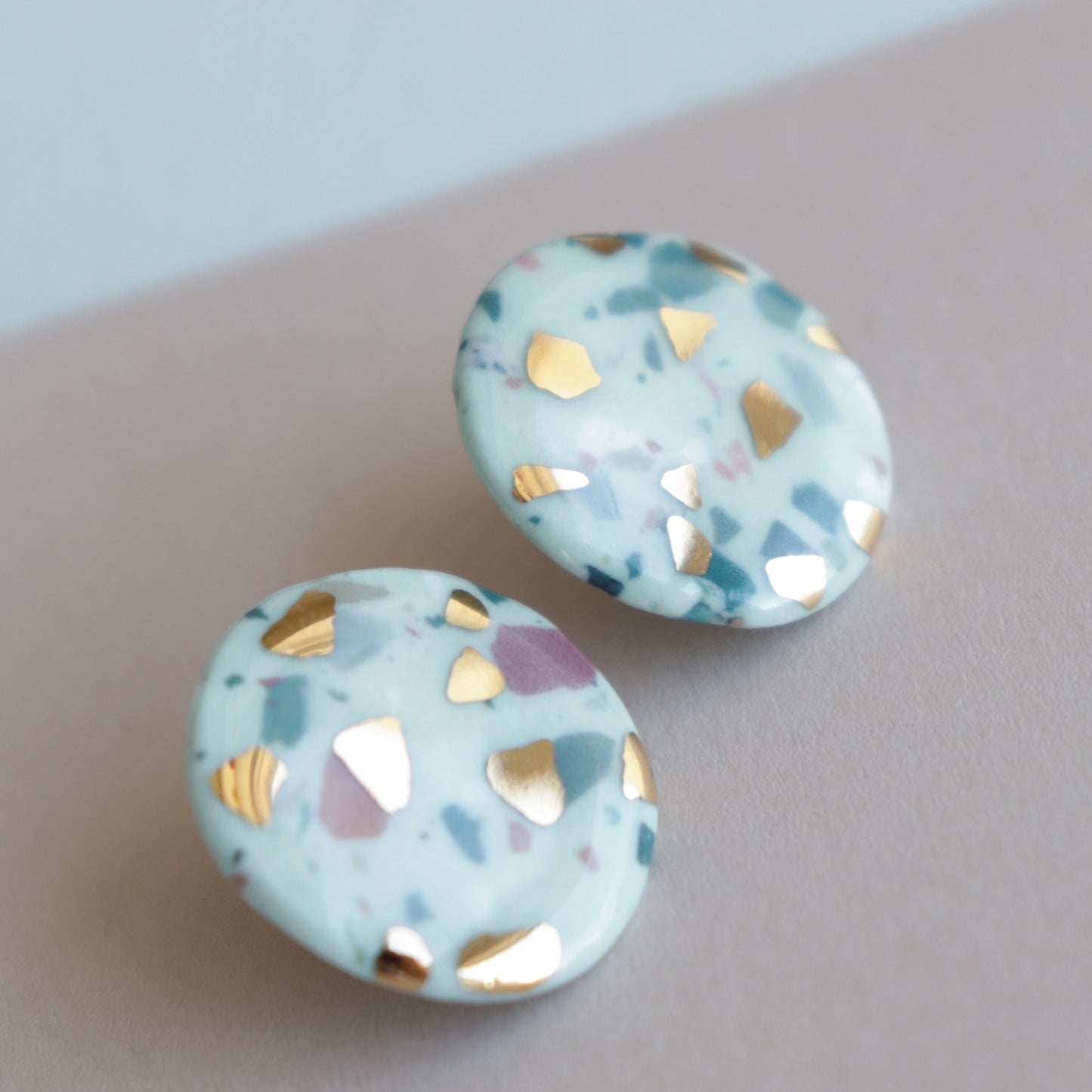 The Astilla Recycled Studs / S by Rozenthal Jewelry feature a terrazzo-style white base with gold, teal, and mauve flecks—an elegant handmade accessory displayed on beige, perfect for elevating any jewelry collection.