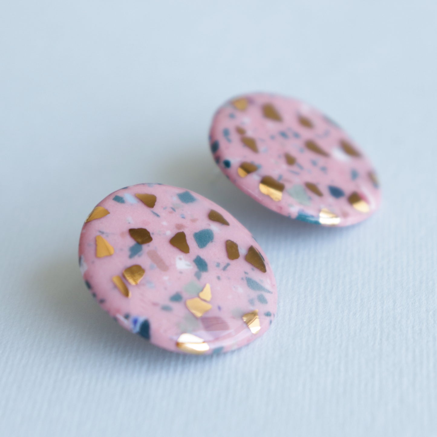 The Astilla Recycled Studs / M by Rozenthal Jewelry are round, pink terrazzo-patterned earrings with gold and dark blue specks—a stunning example of handmade craftsmanship.