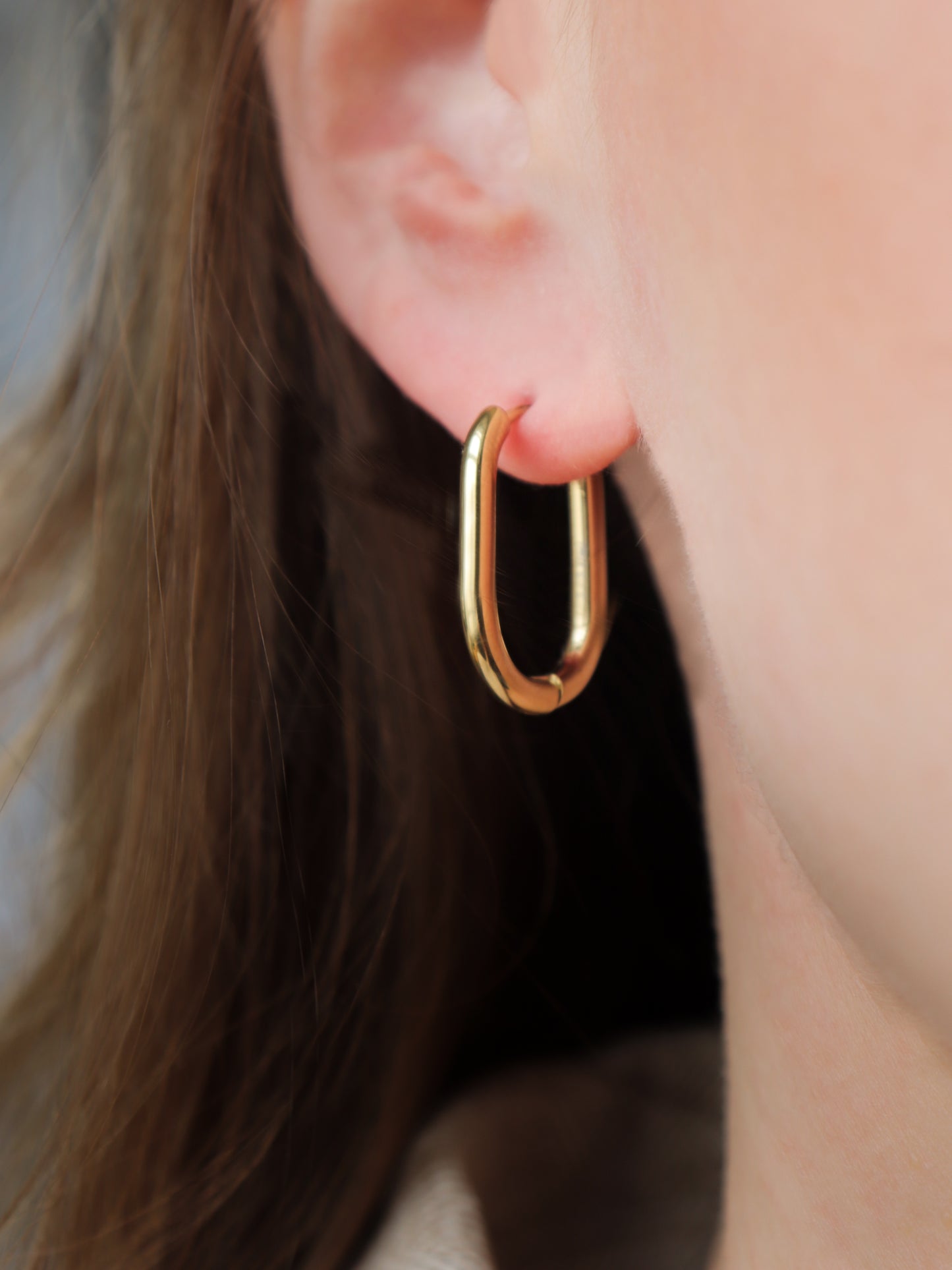 Close-up of a person’s ear wearing Rozenthal Jewelry’s Large Hoops, shiny gold and hypoallergenic. Brown hair is partially visible beside the ear.