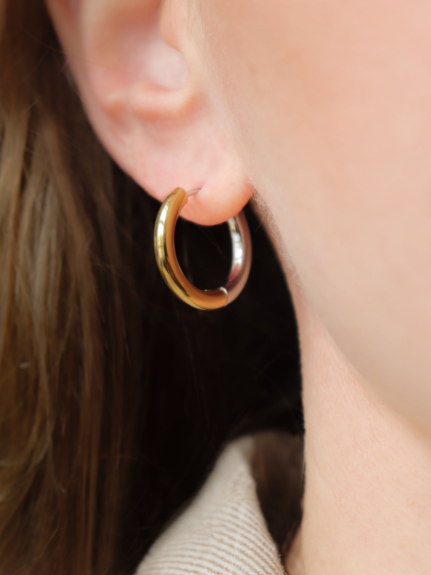 A close-up shows a person wearing Rozenthal Jewelrys Gold and Silver Hoops. Their light brown hair and part of a beige collar are also visible.
