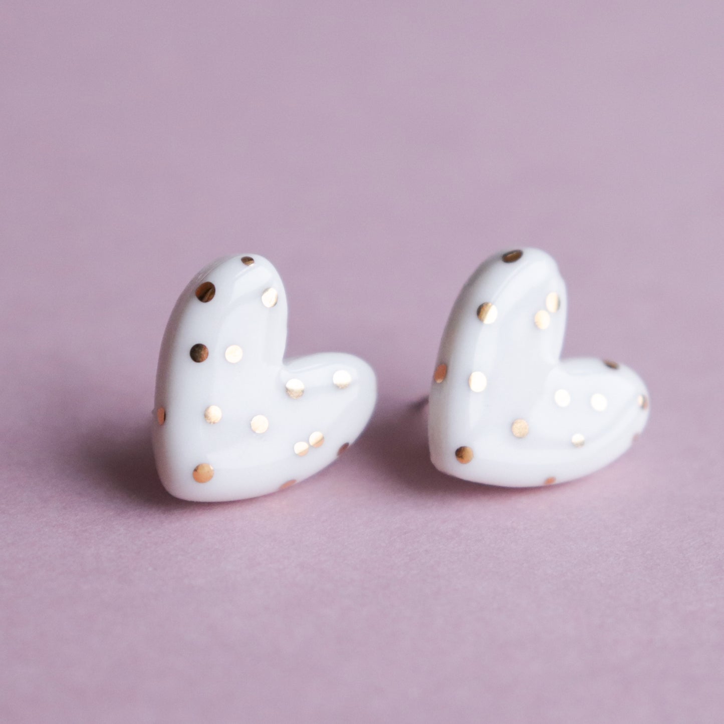 Heart Studs by Rozenthal Jewelry—white porcelain, heart-shaped statement earrings with gold polka dots, shown on a light pink background. A perfect choice for sustainable jewelry lovers for any occasion.