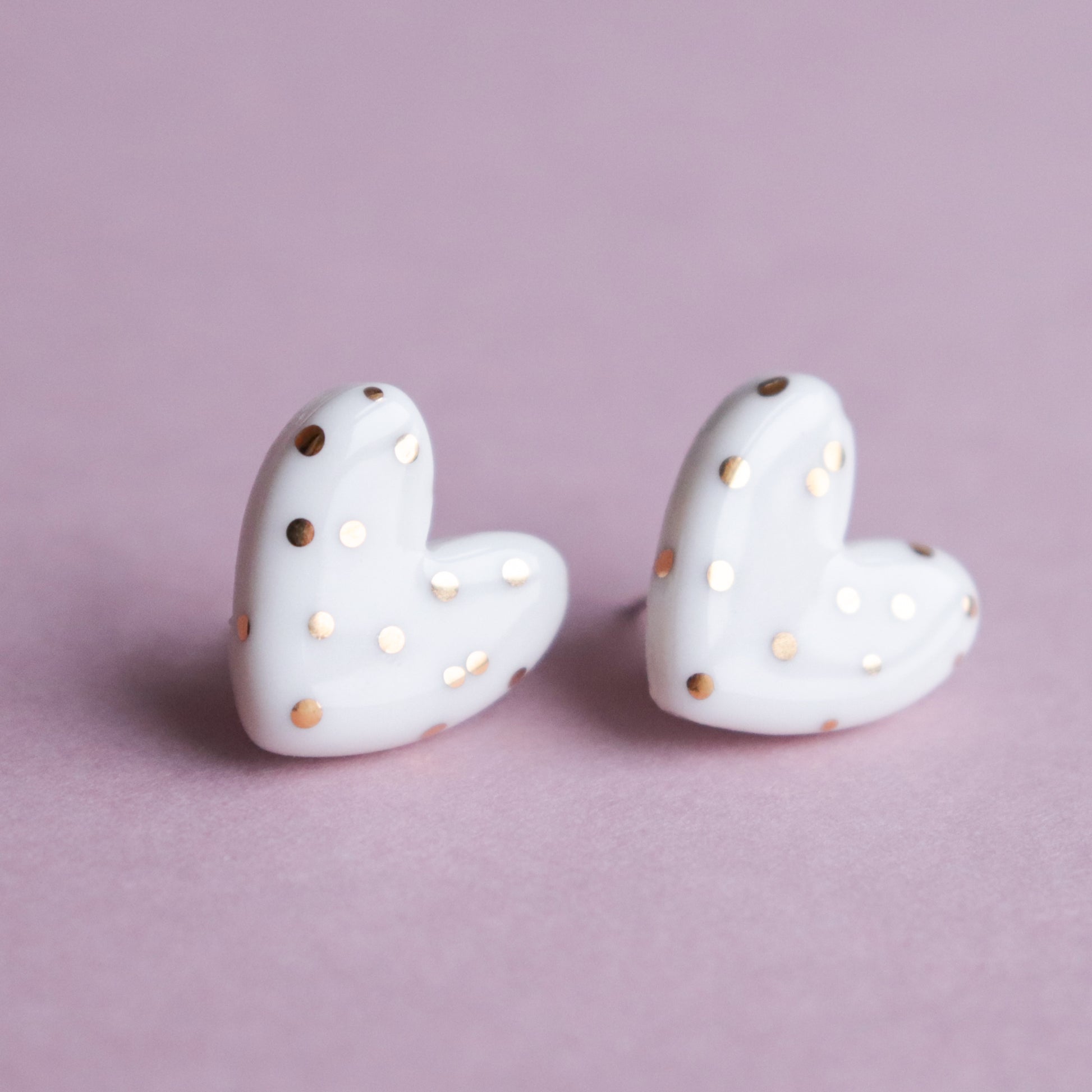 Heart Studs by Rozenthal Jewelry—white porcelain, heart-shaped statement earrings with gold polka dots, shown on a light pink background. A perfect choice for sustainable jewelry lovers for any occasion.