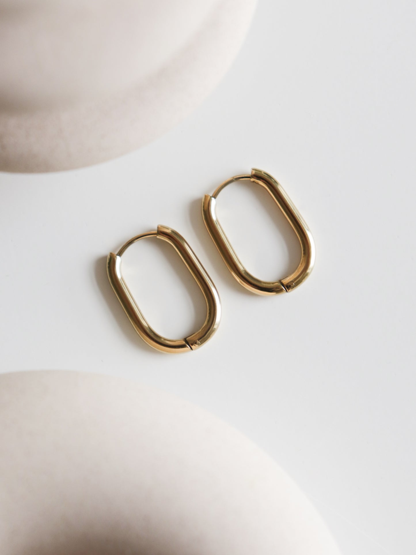 A pair of Large Hoops by Rozenthal Jewelry rests on a smooth white surface, with soft beige shapes blurred in the foreground and background.
