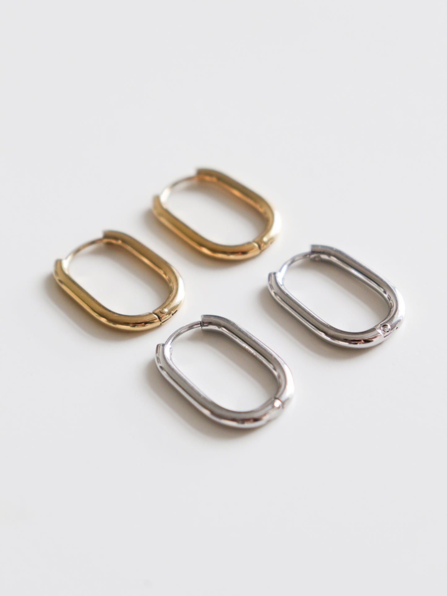 Two pairs of Rozenthal Jewelry Large Hoops—one gold, one silver—rest on a white surface. Crafted from hypoallergenic stainless steel, these earrings blend style and comfort.