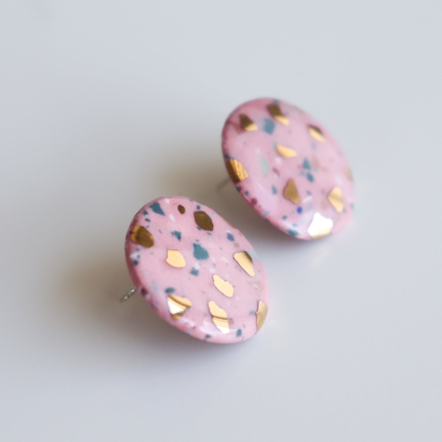 The Astilla Recycled Studs / M by Rozenthal Jewelry are round, pink porcelain earrings with gold flecks and blue speckles, shown on a white background.