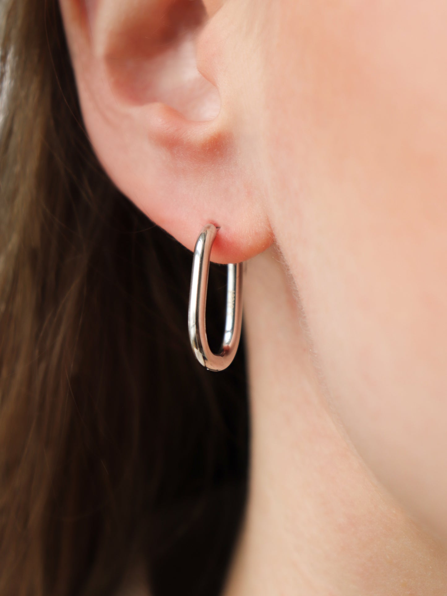 A close-up of a persons ear wearing Rozenthal Jewelrys Large Hoops, simple and shiny stainless steel earrings. Their light skin and partially visible brown hair highlight these waterproof hoops—perfect for everyday wear.