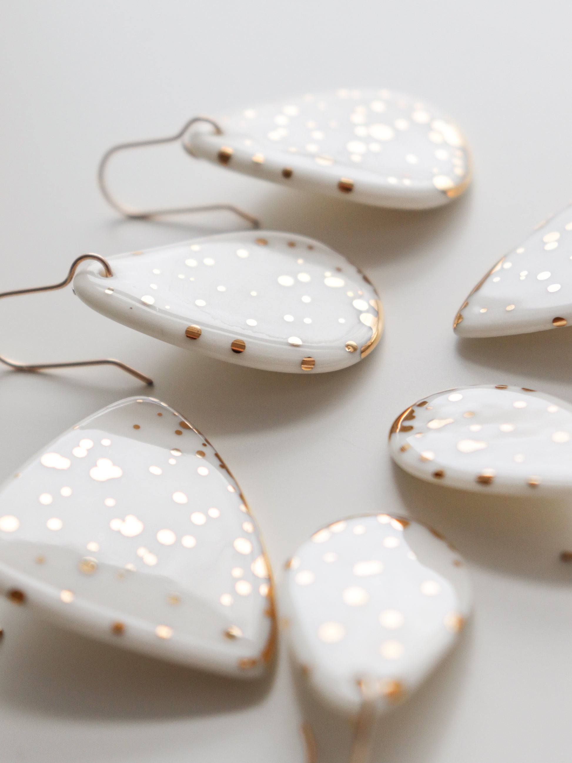 Close-up of Rozenthal Jewelry’s Drop Earrings / S—handmade in Latvia with white ceramic, gold speckles, and edges. The teardrop and triangle shapes have minimalist hooks, offering elegant, sustainable style.