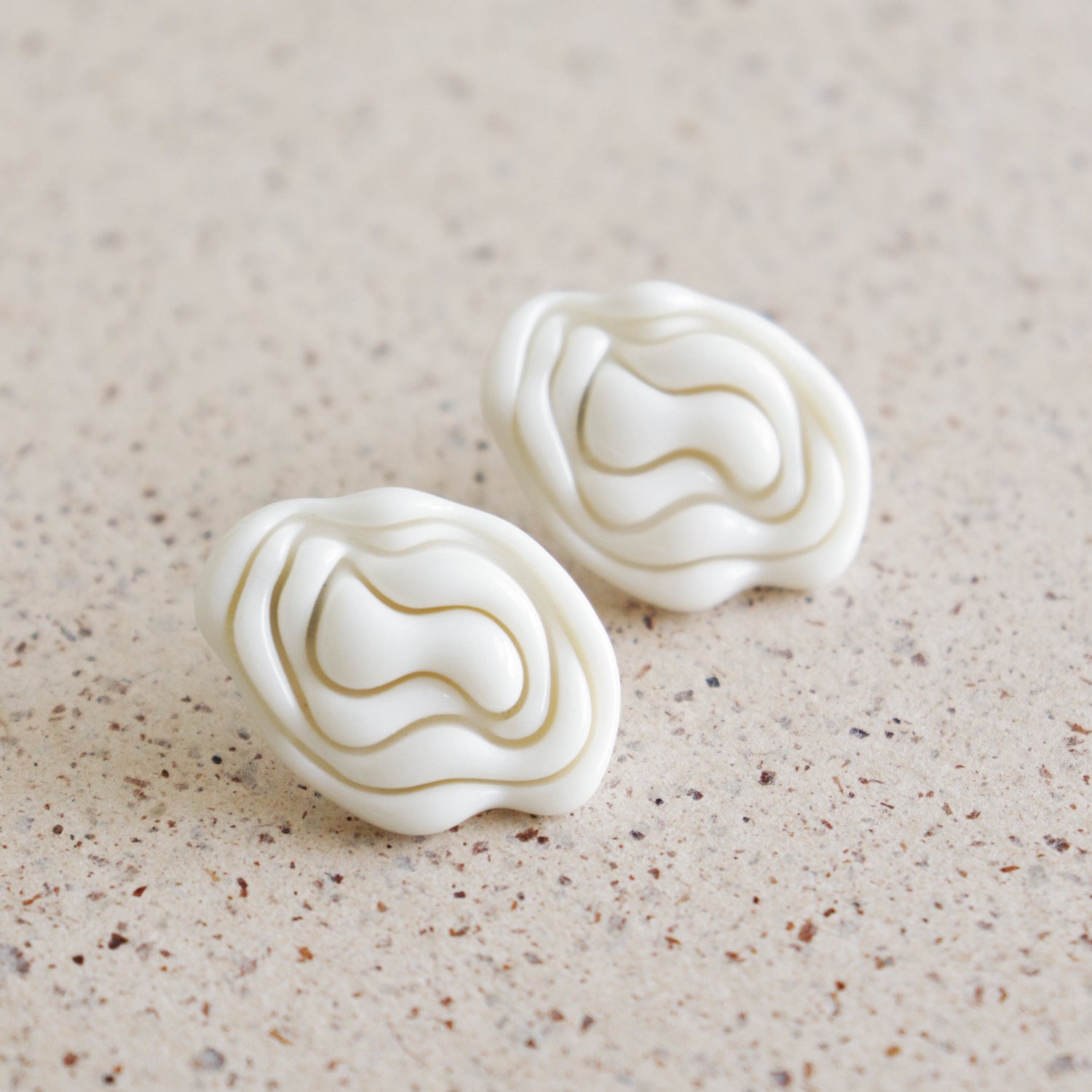 Pair of white textured earrings on a beige surface
