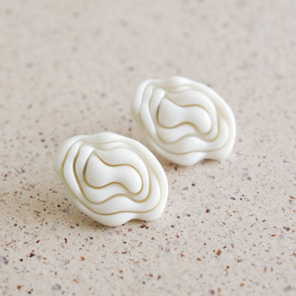 Pair of white textured earrings on a beige surface