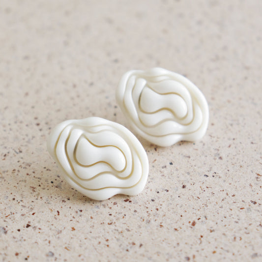 Pair of white textured earrings on a beige surface